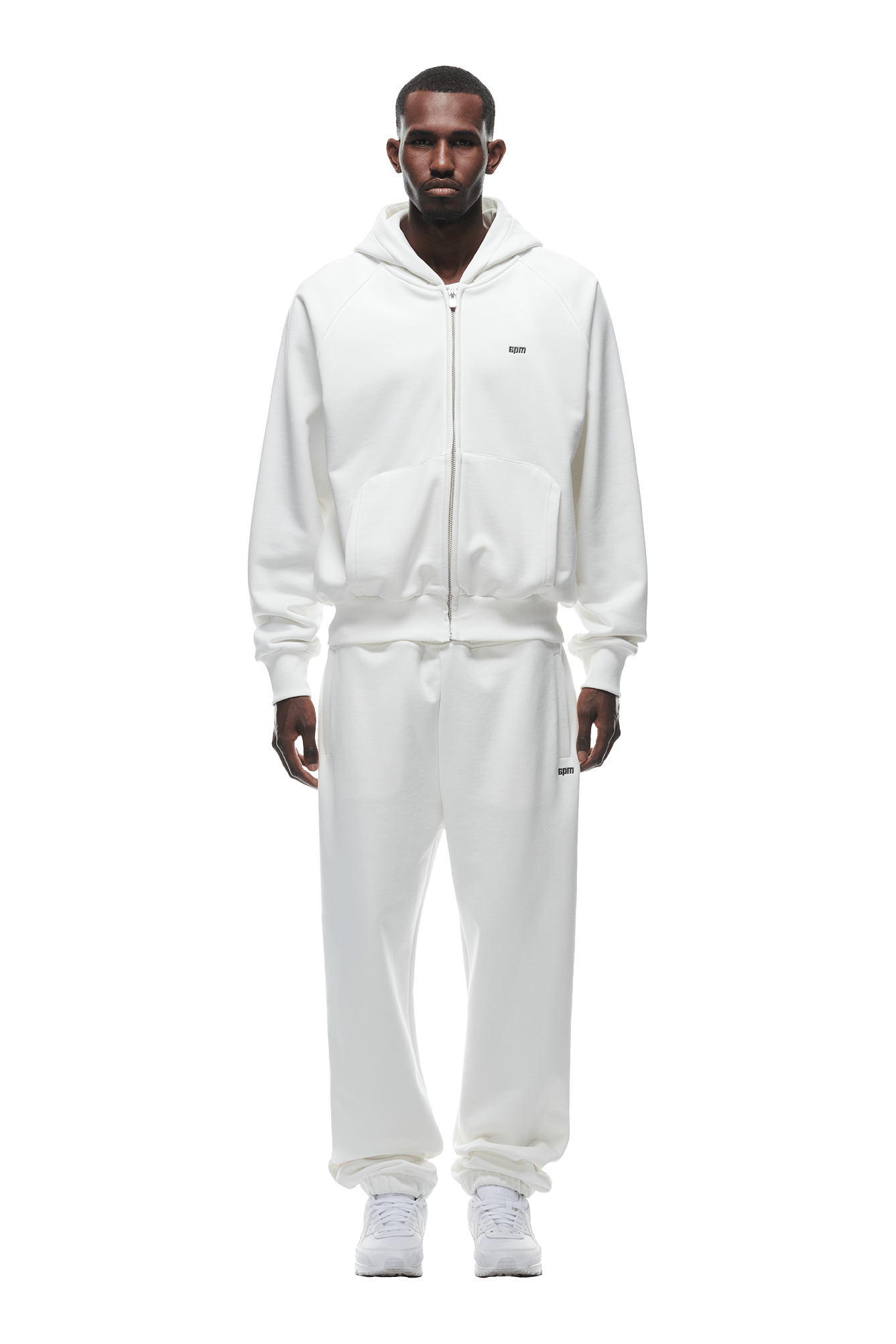 A man faces forward in a 6PM ZIP HOODIE COCONUT WHITE with matching white sweatpants and sneakers, set against a plain background, creating a clean, everyday-ready look.