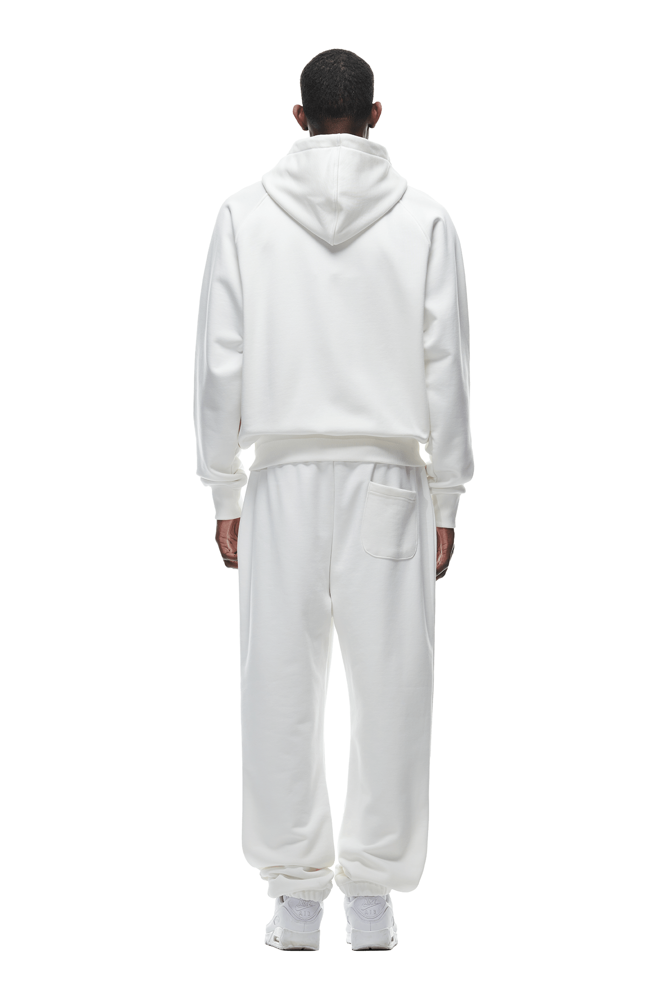 A person faces away, wearing the 6PM ZIP HOODIE COCONUT WHITE with matching sweatpants and white sneakers against a plain background, highlighting the hoodie’s clean finish—ideal for everyday wear.