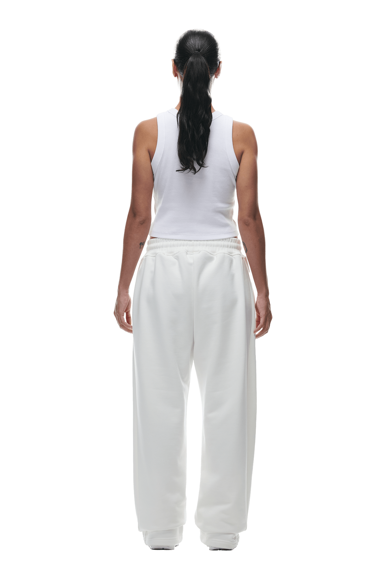 A person with long dark hair in a ponytail stands facing away against a plain green background, wearing the 6PM OPEN LEG JOGGER COCONUT WHITE.