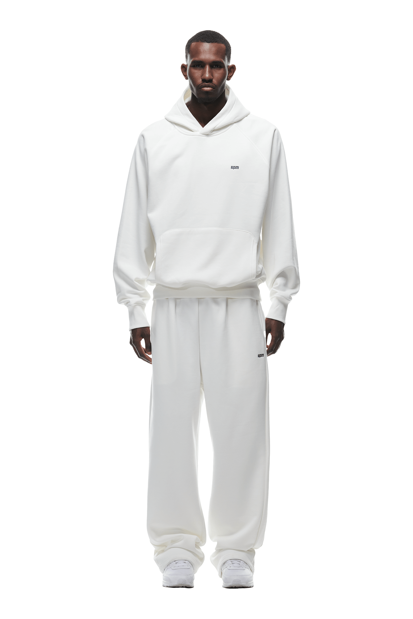 A man stands facing forward, wearing 6PM’s HOODIE COCONUT WHITE with raglan sleeves and a kangaroo pocket, paired with matching white sweatpants and sneakers. The comfy everyday look appears against a transparent background.