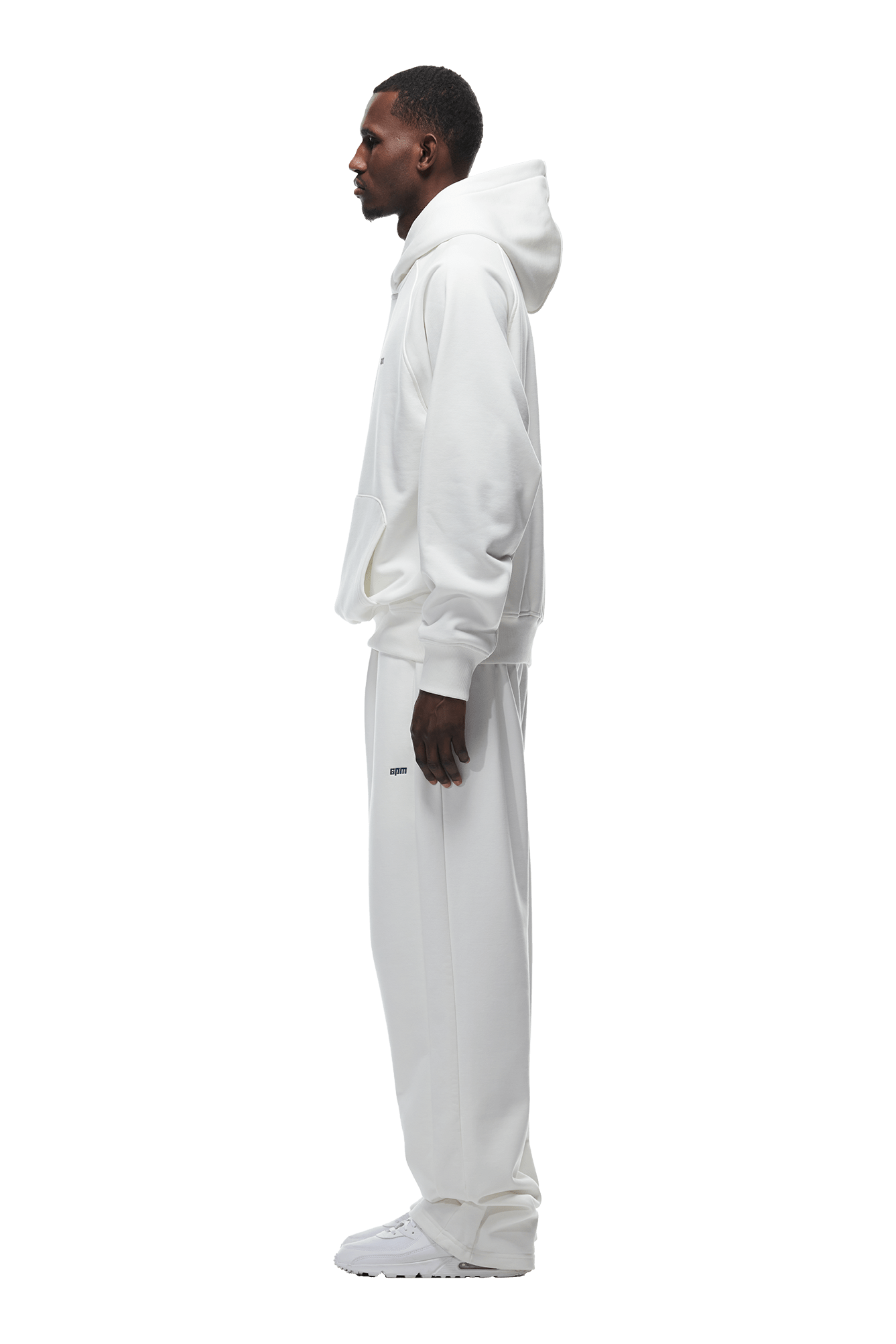 A man in profile wears the 6PM HOODIE COCONUT WHITE, featuring raglan sleeves and a kangaroo pocket, paired with matching white sweatpants and sneakers—an ideal everyday outfit, shown on a transparent background.