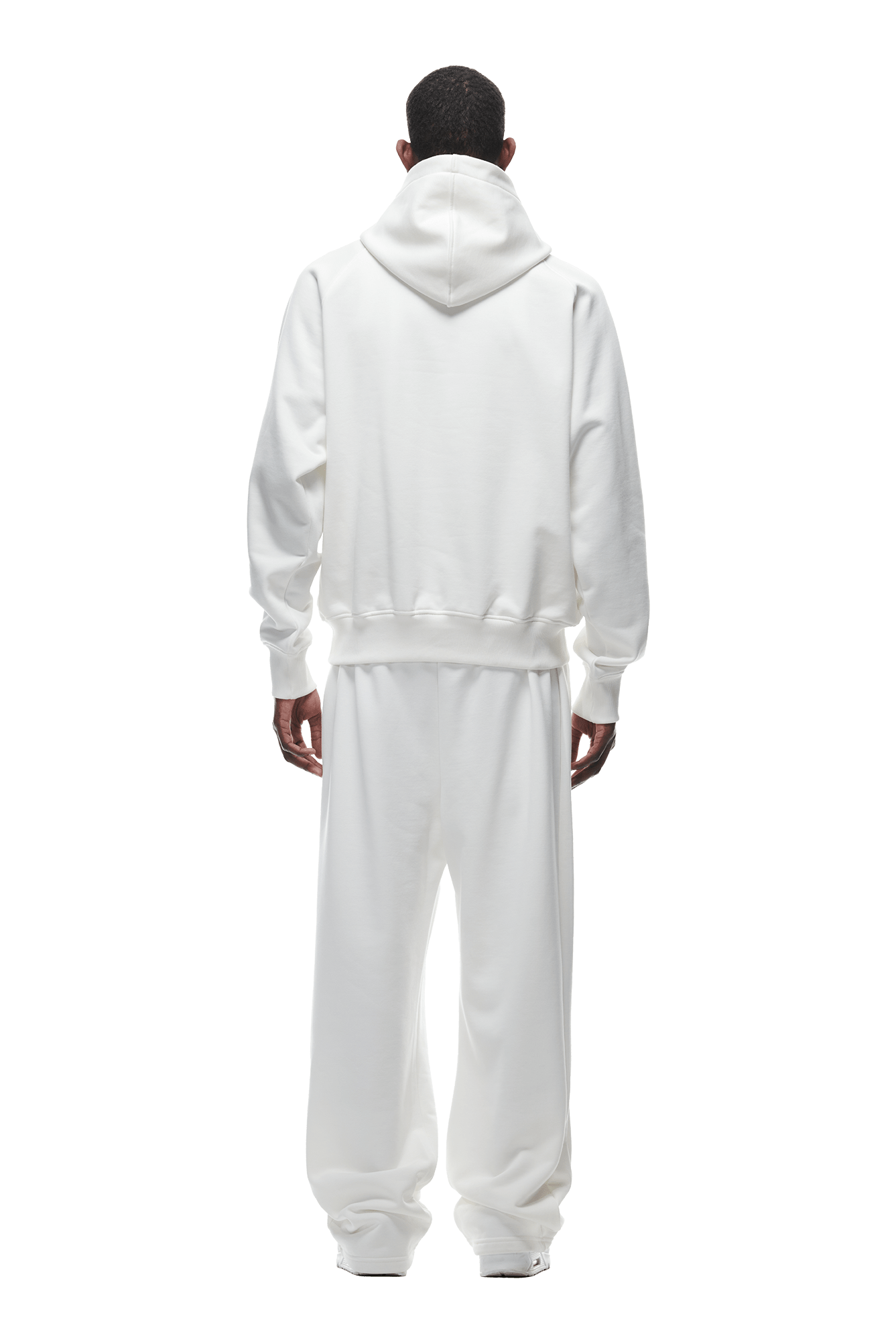 A person faces away, wearing the 6PM HOODIE COCONUT WHITE with matching white sweatpants—loose-fitting and ideal for daily wear—standing with relaxed hands against a plain, transparent background.