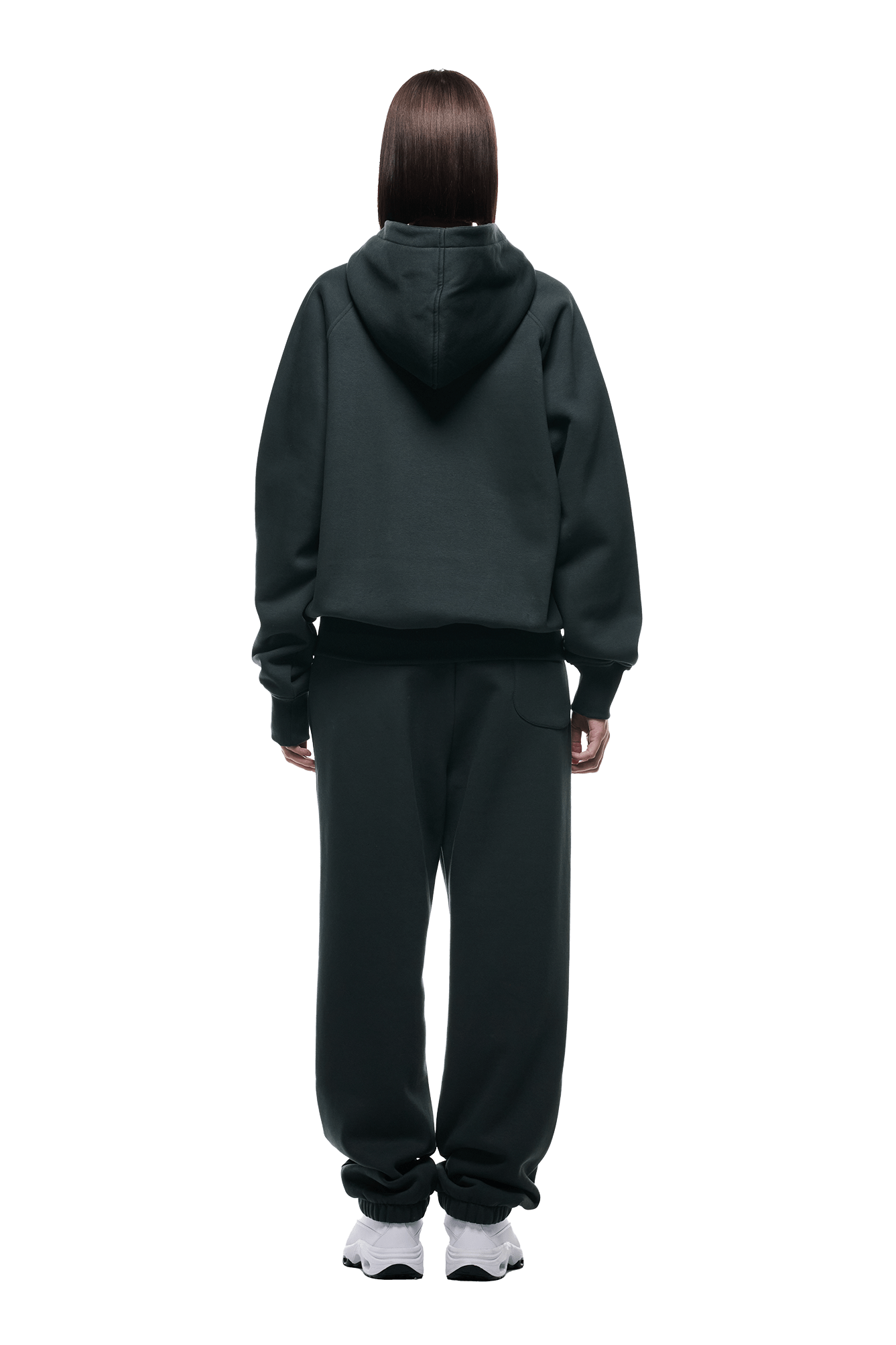 A person with straight brown hair faces away, wearing the 6PM ZIP HOODIE DARK EMERALD and matching sweatpants with white sneakers—perfect for everyday use, set against a plain background.