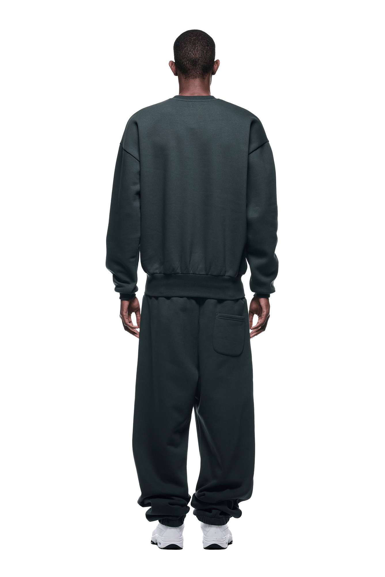 A person stands facing away, wearing the 6PM CREWNECK DARK EMERALD sweatshirt and matching sweatpants with a patch pocket, paired with white sneakers against a plain background.