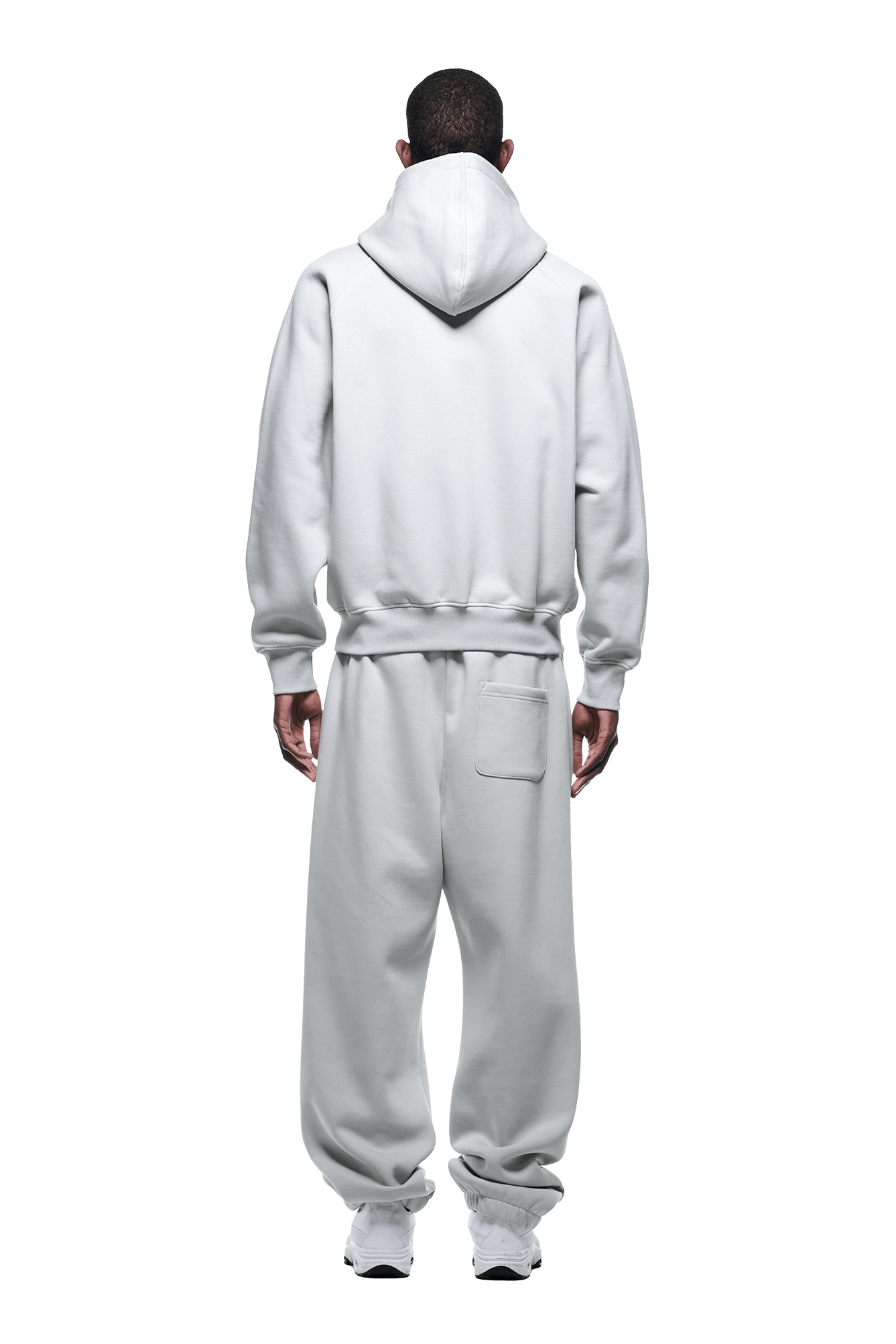 A person faces away in a 6PM ZIP HOODIE SMOKE GREY and matching sweatpants with a back pocket, finished for daily wear. The hood is up, white sneakers complete the outfit, and the background is transparent.