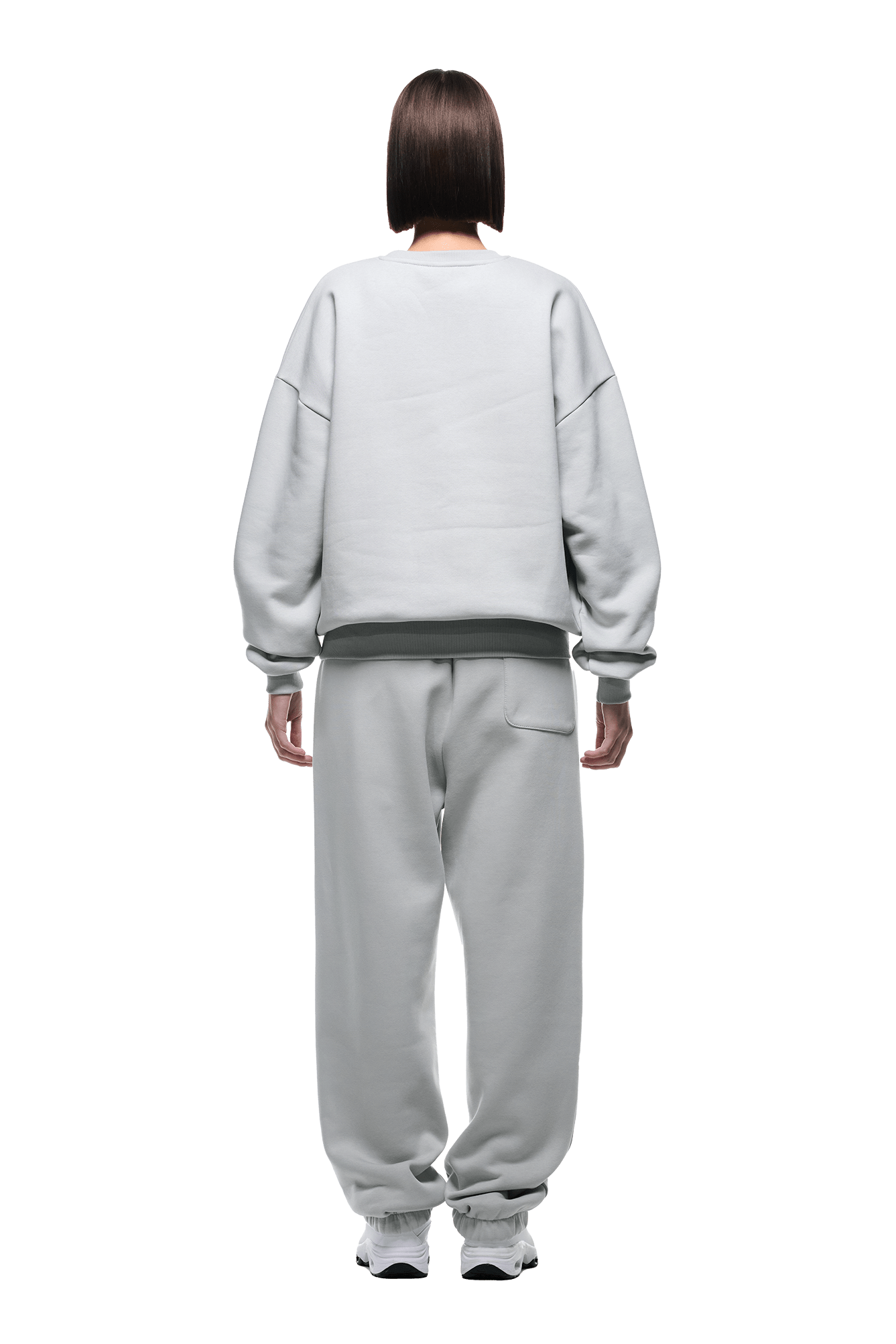 A person with chin-length brown hair, seen from behind, wears the 6PM CREWNECK SMOKE GREY sweatshirt and matching sweatpants with white sneakers, standing against a plain background.