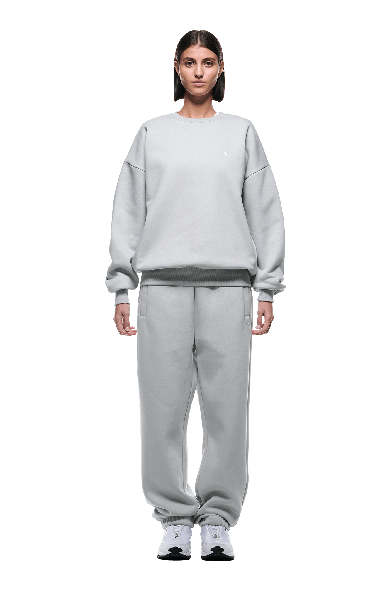 A person stands facing forward, wearing the 6PM CREWNECK SMOKE GREY sweatshirt and matching sweatpants with white sneakers, against a plain green background.