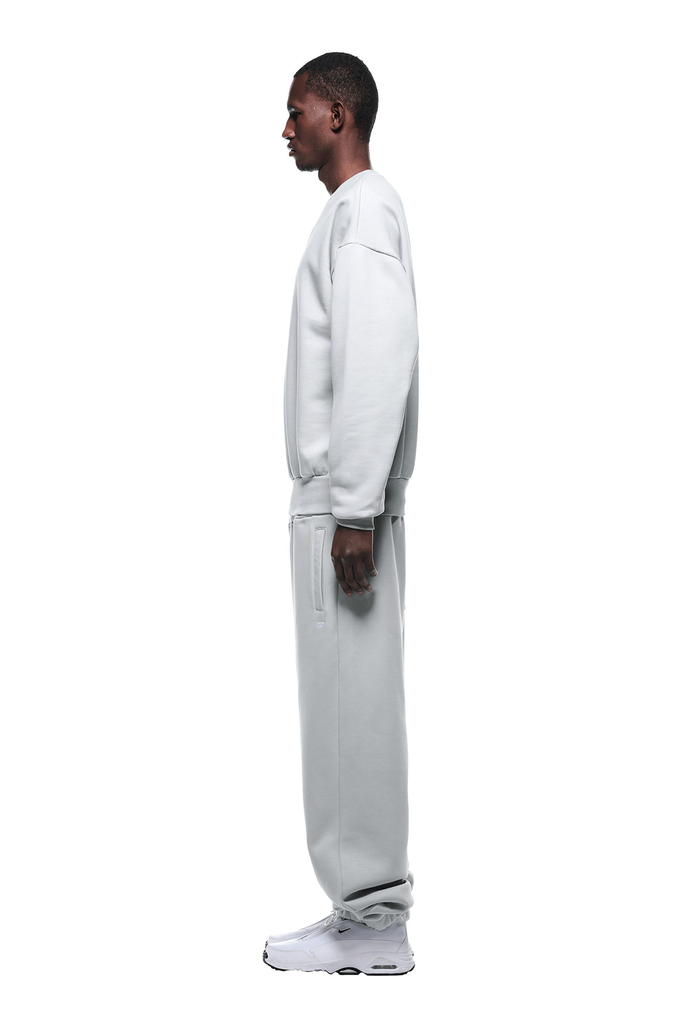 A man stands in profile, wearing the 6PM CREWNECK SMOKE GREY sweatshirt paired with matching sweatpants and white sneakers, set against a transparent background.