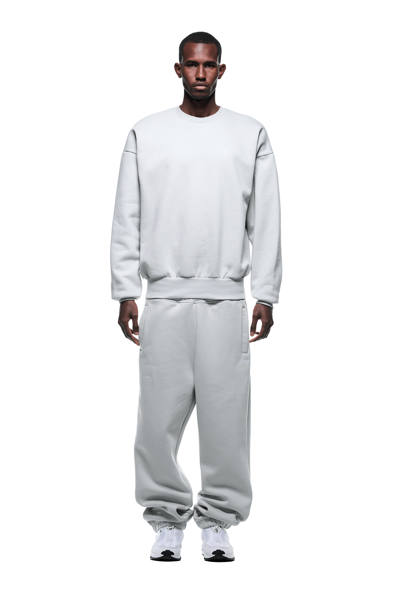 A man faces forward wearing the 6PM CREWNECK SMOKE GREY sweatshirt, featuring a boxy fit and ribbed trims, paired with matching sweatpants and white sneakers against a plain background.