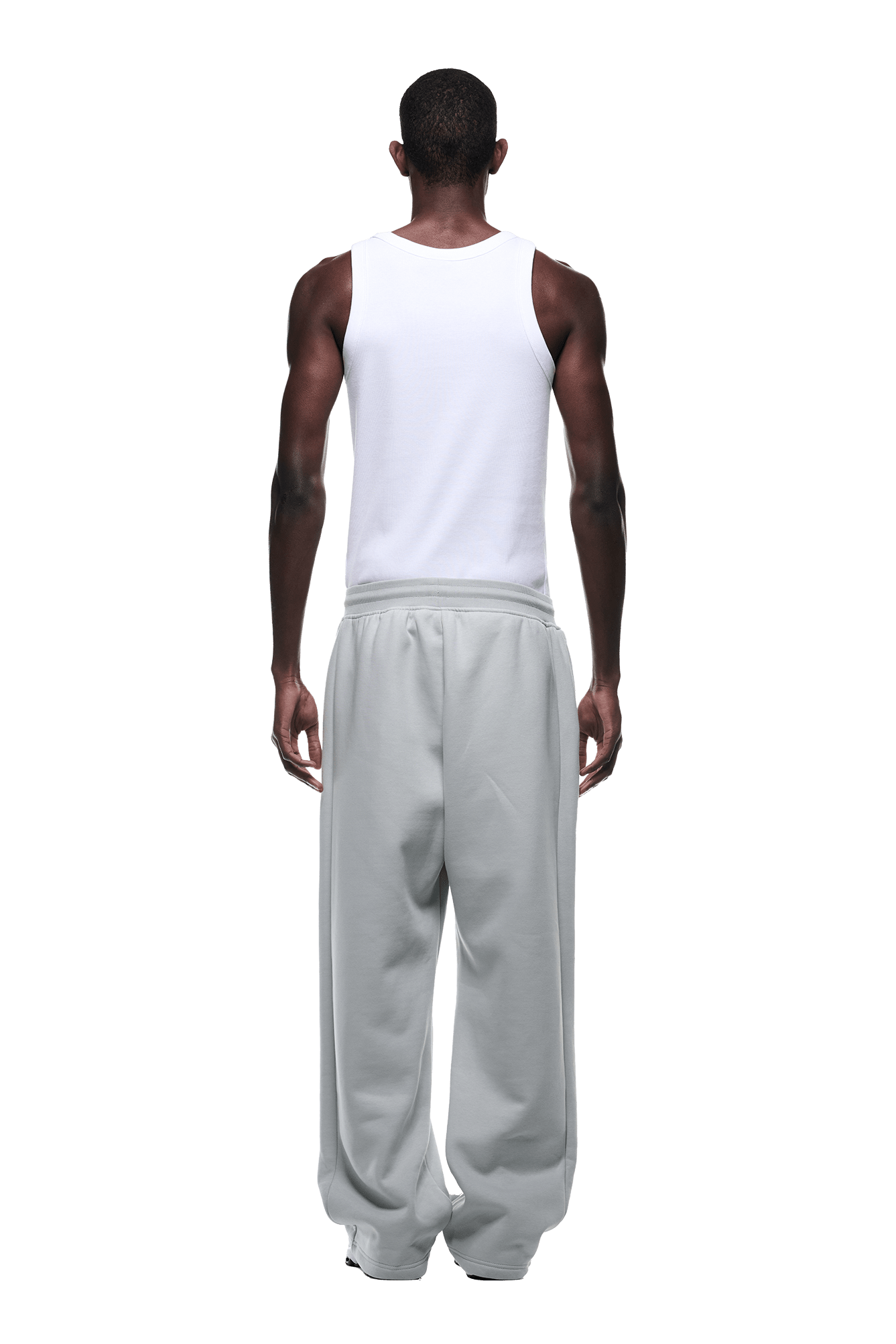 A man faces away from the camera, wearing a white sleeveless tank and OPEN LEG JOGGER SMOKE GREY sweatpants with a stacking length. The modern classic look is set against a transparent background.