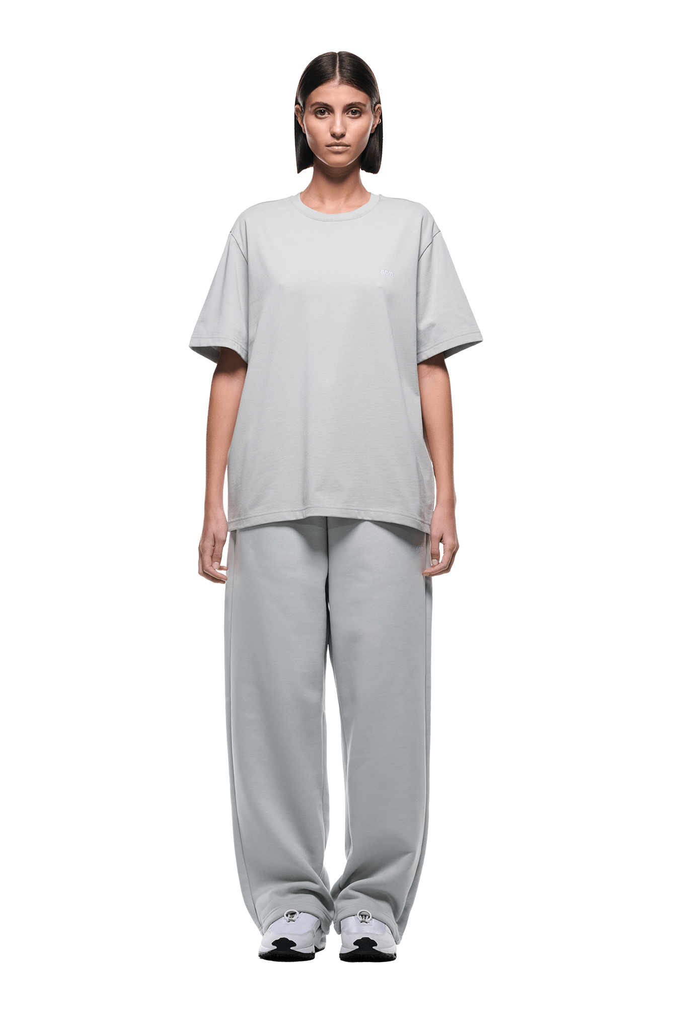 A person stands facing forward, wearing the 6PM T-SHIRT SMOKE GREY with matching baggy pants and white sneakers, set against a plain green background.