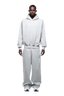 A man stands facing forward in a HOODIE SMOKE GREY with raglan sleeves and a kangaroo pocket, matching sweatpants, and white sneakers. Against a transparent background, his hands rest at his sides, highlighting this everyday outfit.