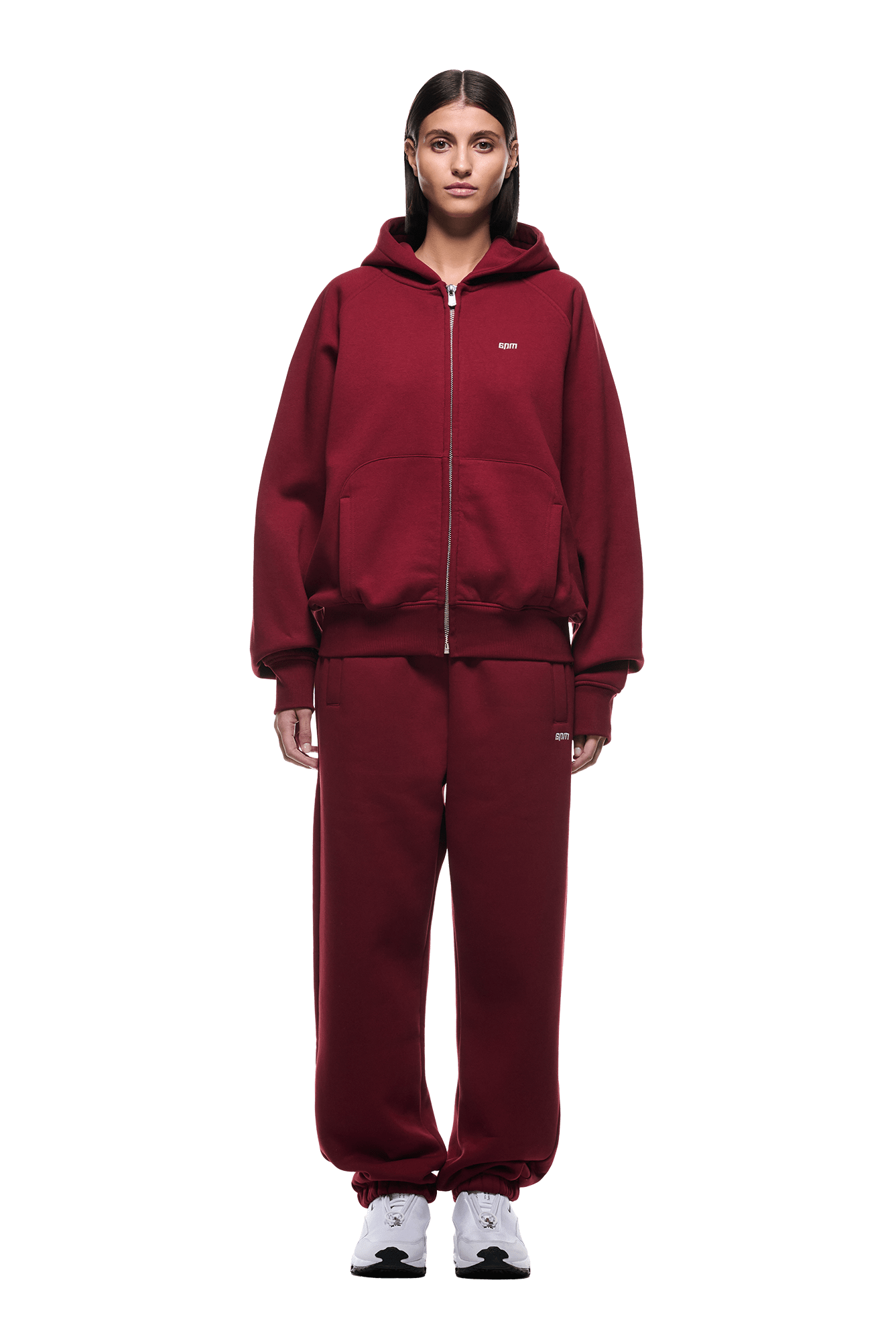 A person stands facing forward, wearing the 6PM ZIP HOODIE WINE RED and matching sweatpants with white sneakers. The zipped hoodie offers a clean finish and comfort for everyday wear. The background is transparent.