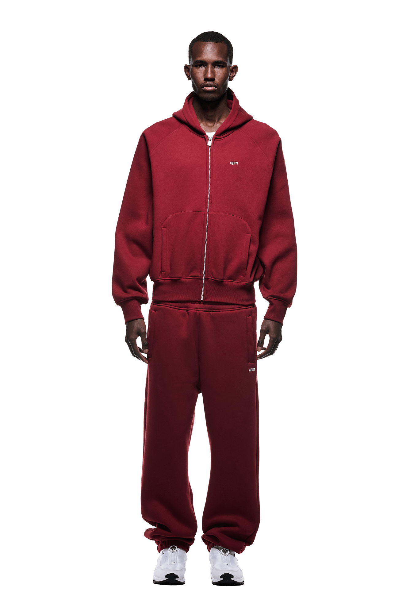 A person stands facing forward in the 6PM ZIP HOODIE WINE RED and matching sweatpants with white sneakers. The outfit offers a clean finish for daily wear, set against a transparent background.