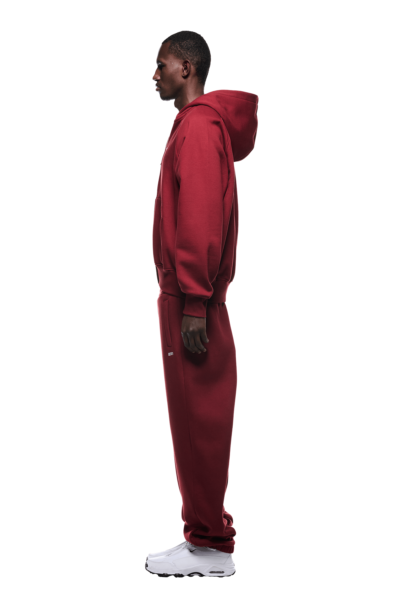 A man in profile wears the 6PM ZIP HOODIE WINE RED set with white sneakers, presenting a clean look ideal for everyday wear against a plain green background.