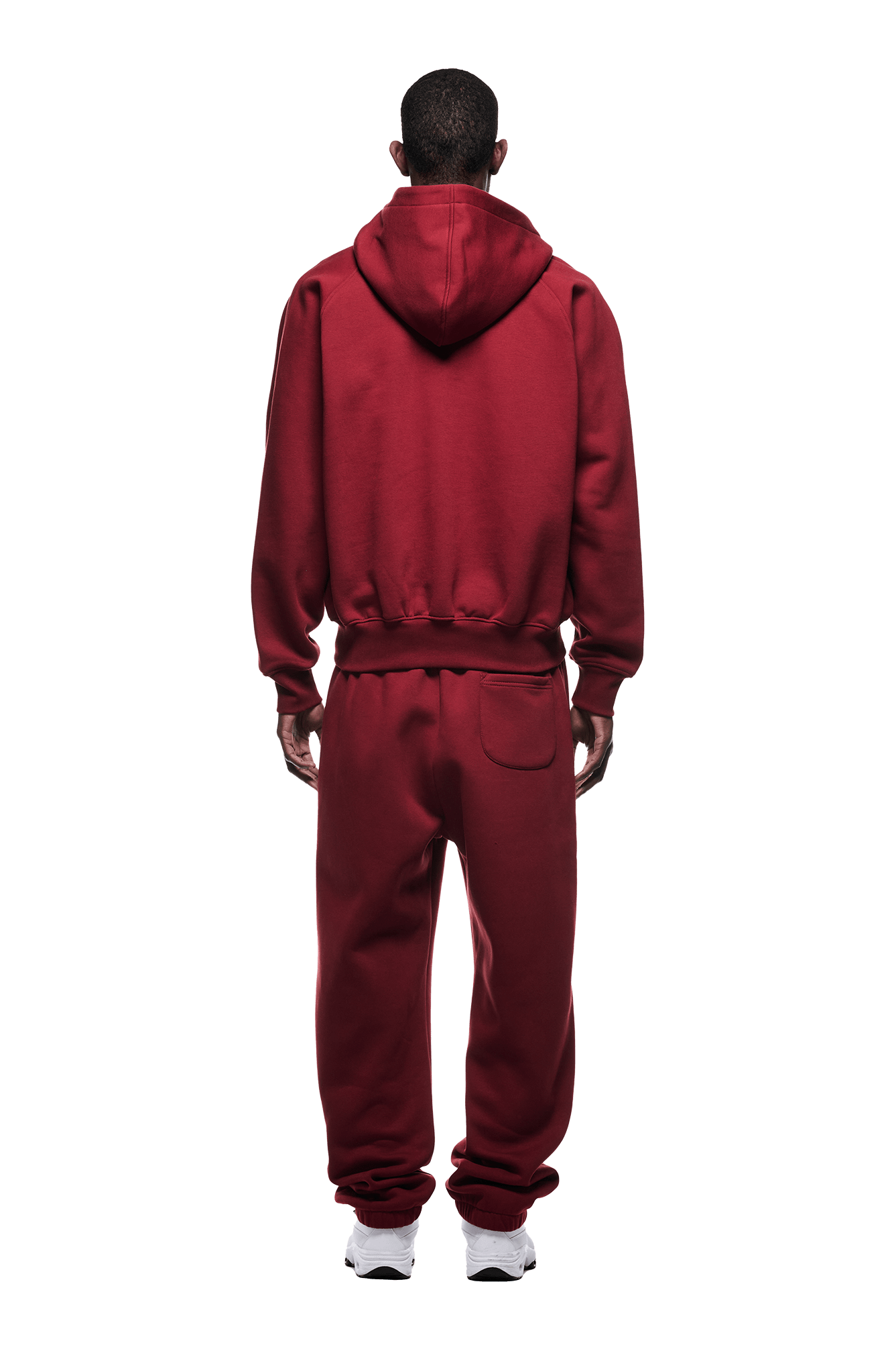 A person faces away, wearing the 6PM ZIP HOODIE WINE RED with matching sweatpants and white sneakers, highlighting its clean finish and structured feel against a plain backdrop.