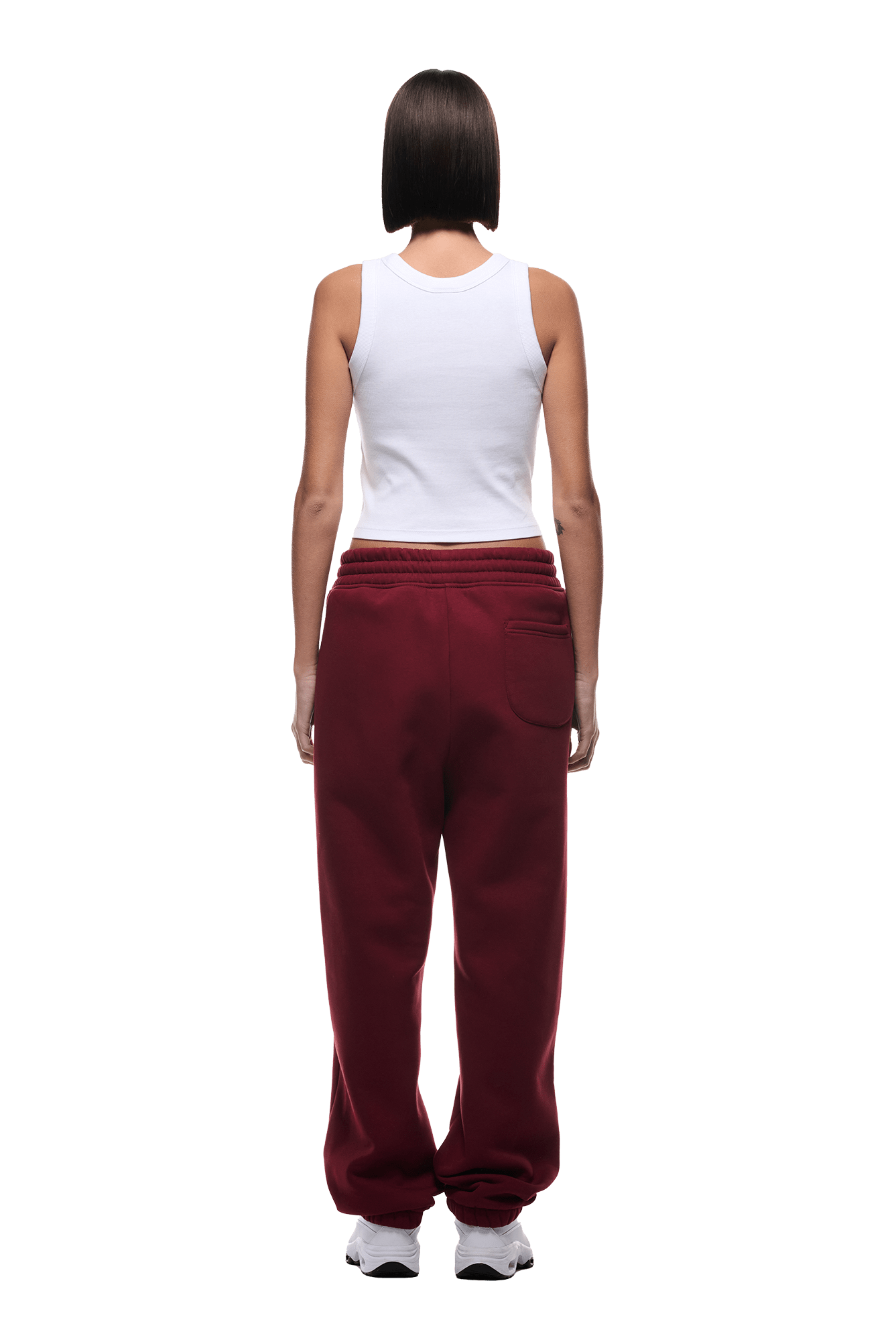 A person with short dark hair, wearing a classic fit white sleeveless top, 6PM CUFF JOGGER WINE RED sweatpants with cuffed legs, and white sneakers stands facing away from the camera against a plain background.