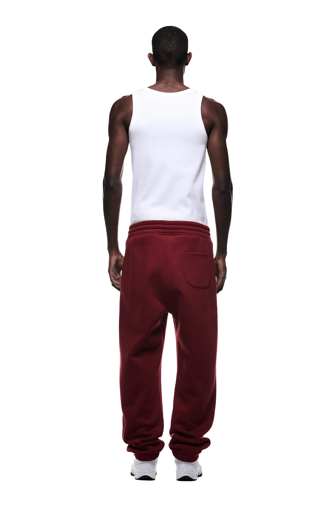 A man faces away, wearing a white tank top and 6PM CUFF JOGGER WINE RED sweatpants with cuffed legs and a back pocket, paired with white sneakers against a plain green background.