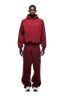 A man faces forward in the HOODIE WINE RED, a matching dark red raglan-sleeved hoodie with kangaroo pocket and sweatpants, paired with white sneakers. The look is ideal for daily wear. Background is transparent.