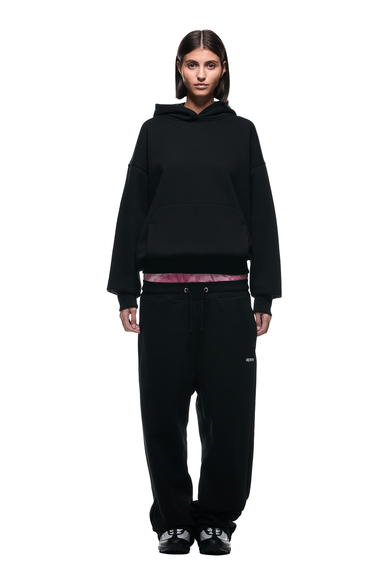 A person stands facing forward against a plain white background, wearing the 6PM DOT CAMO LETTER HOODIE BLACK, paired with black sweatpants, black sneakers, and a visible burgundy waistband.