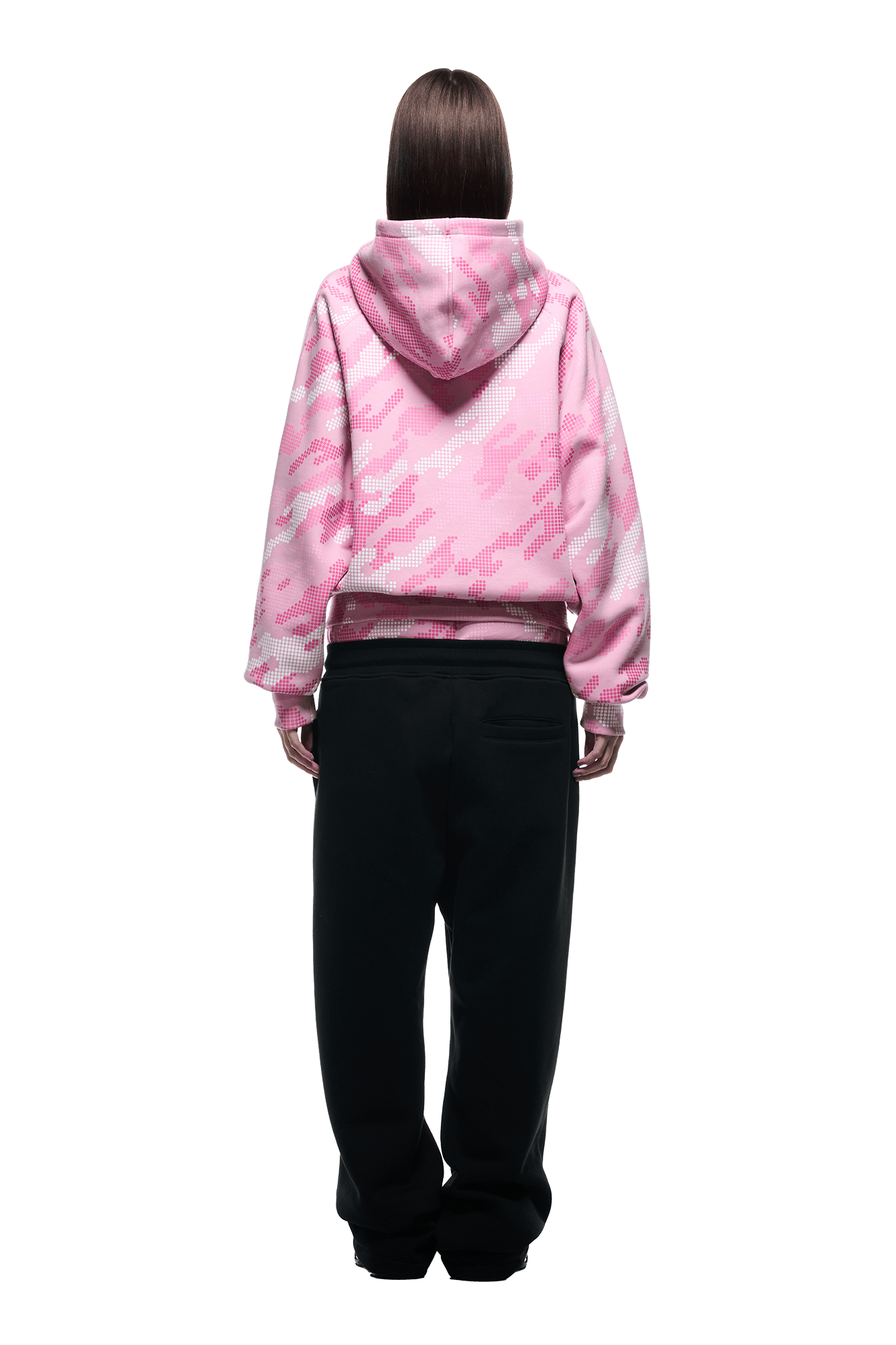 A person stands facing away, wearing the 6PM DOT CAMO ZIP HOODIE PINK with the hood up and loose black pants, set against a plain white background.