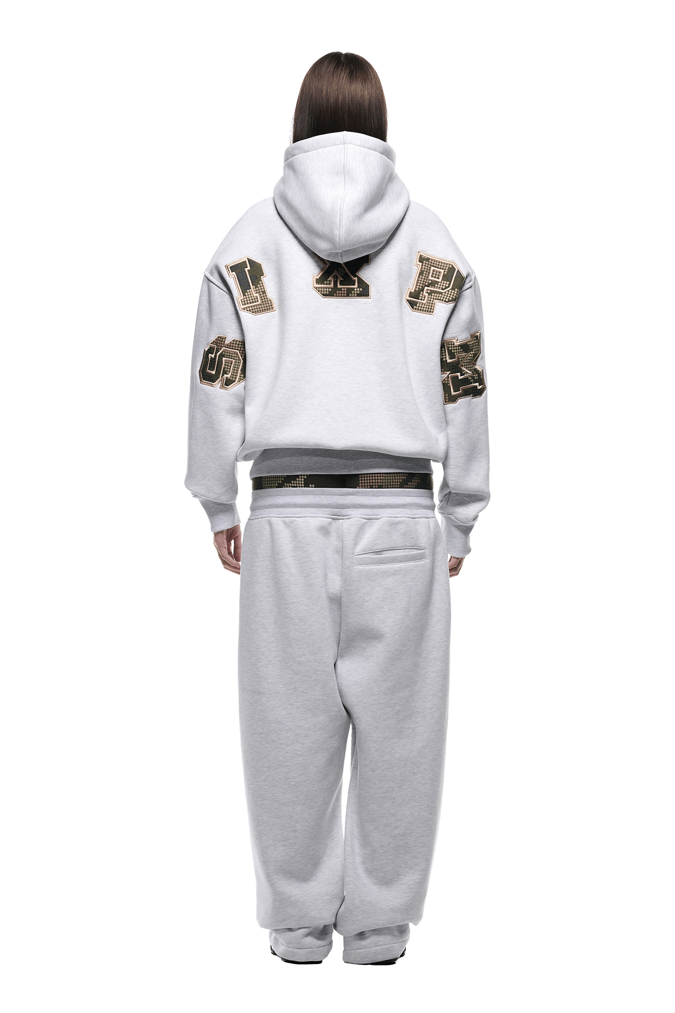 A person faces away in a 6PM DOT CAMO LETTER HOODIE GREY, featuring large black and gold varsity-style patches on the back and sleeves. They wear matching sweatpants against a plain white background.
