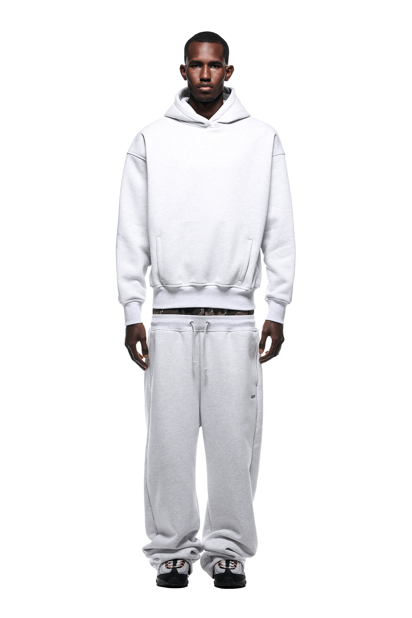 A man faces forward against a white background, wearing the 6PM DOT CAMO LETTER HOODIE GREY and matching baggy sweatpants with black sneakers.