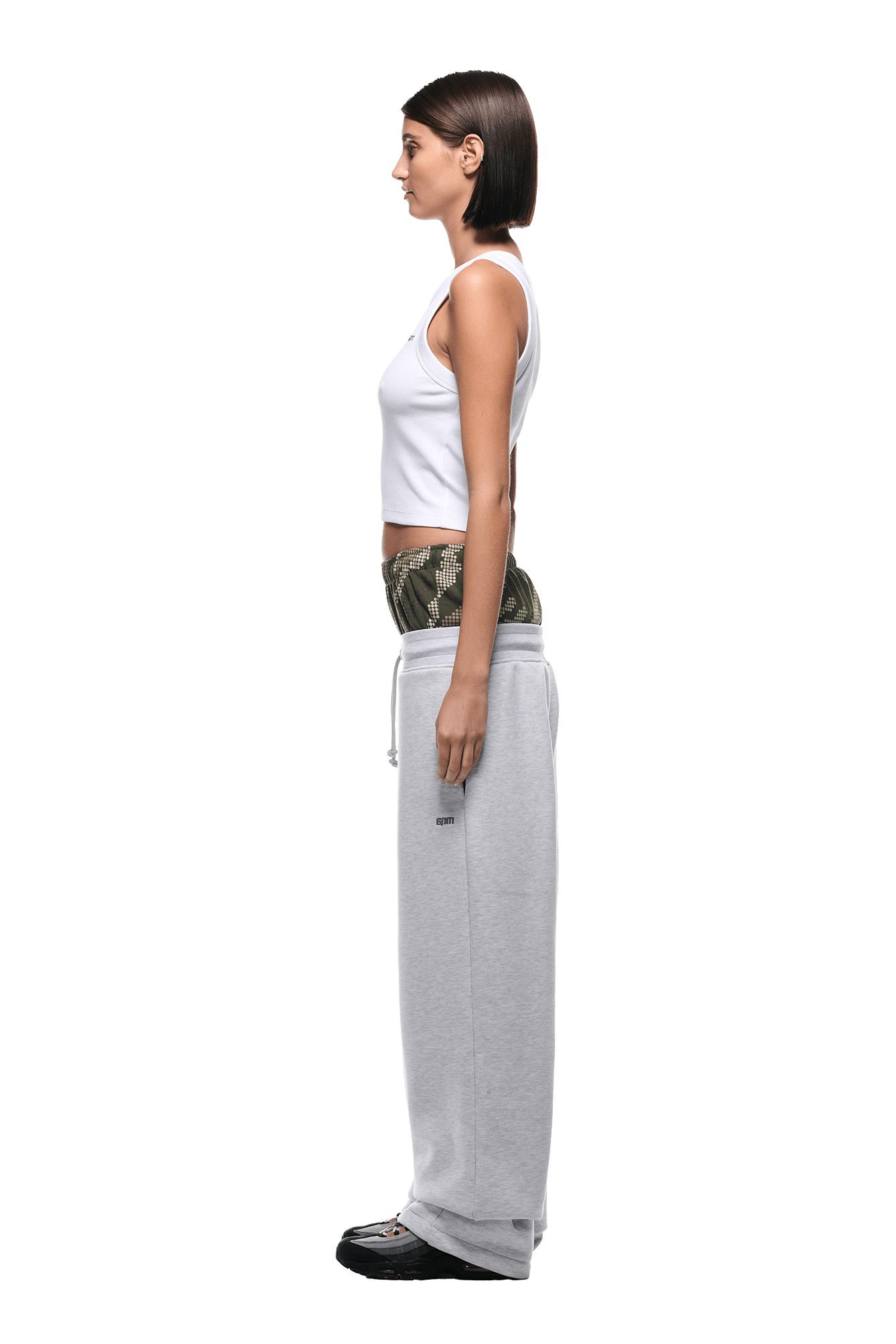 A woman in profile stands straight with arms at her sides, wearing 6PM BOXERS OPEN LEG JOGGER GREY sweatpants pulled down below the hips, a white tank top, and patterned briefs against a transparent background.