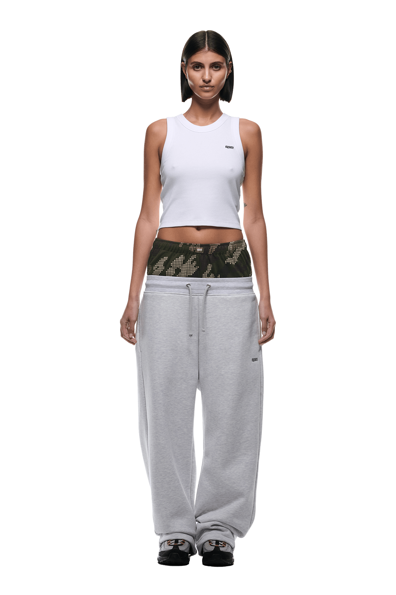 A woman faces forward wearing a white sleeveless crop top, black sneakers, and 6PM BOXERS OPEN LEG JOGGER GREY sweatpants with a wide waistband. She has short, straight hair and a neutral expression on a transparent background.