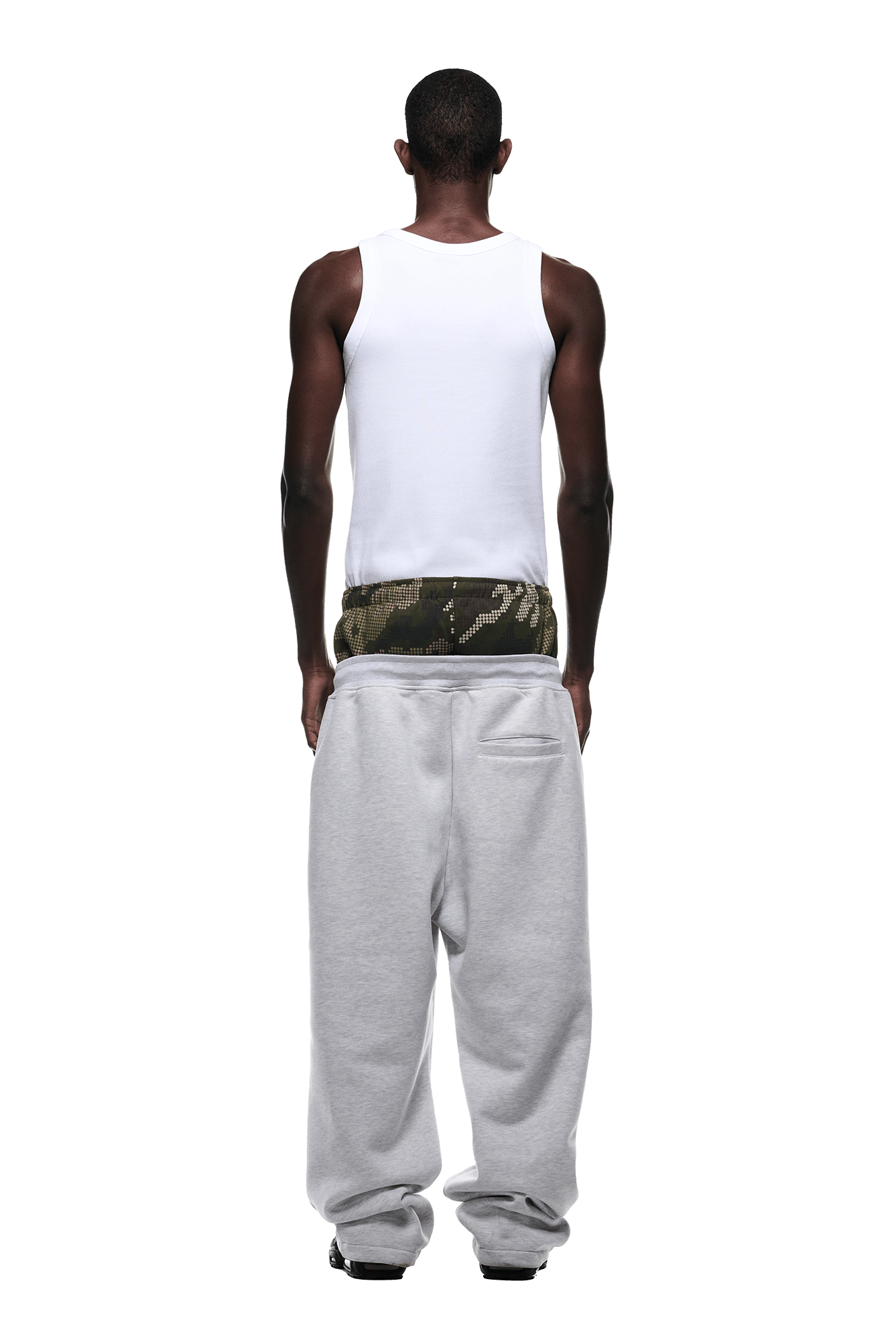 A person faces away against a solid green background, wearing gray 6PM BOXERS OPEN LEG JOGGER pants with camouflage-patterned underwear visible above the waistband and a white tank top.
