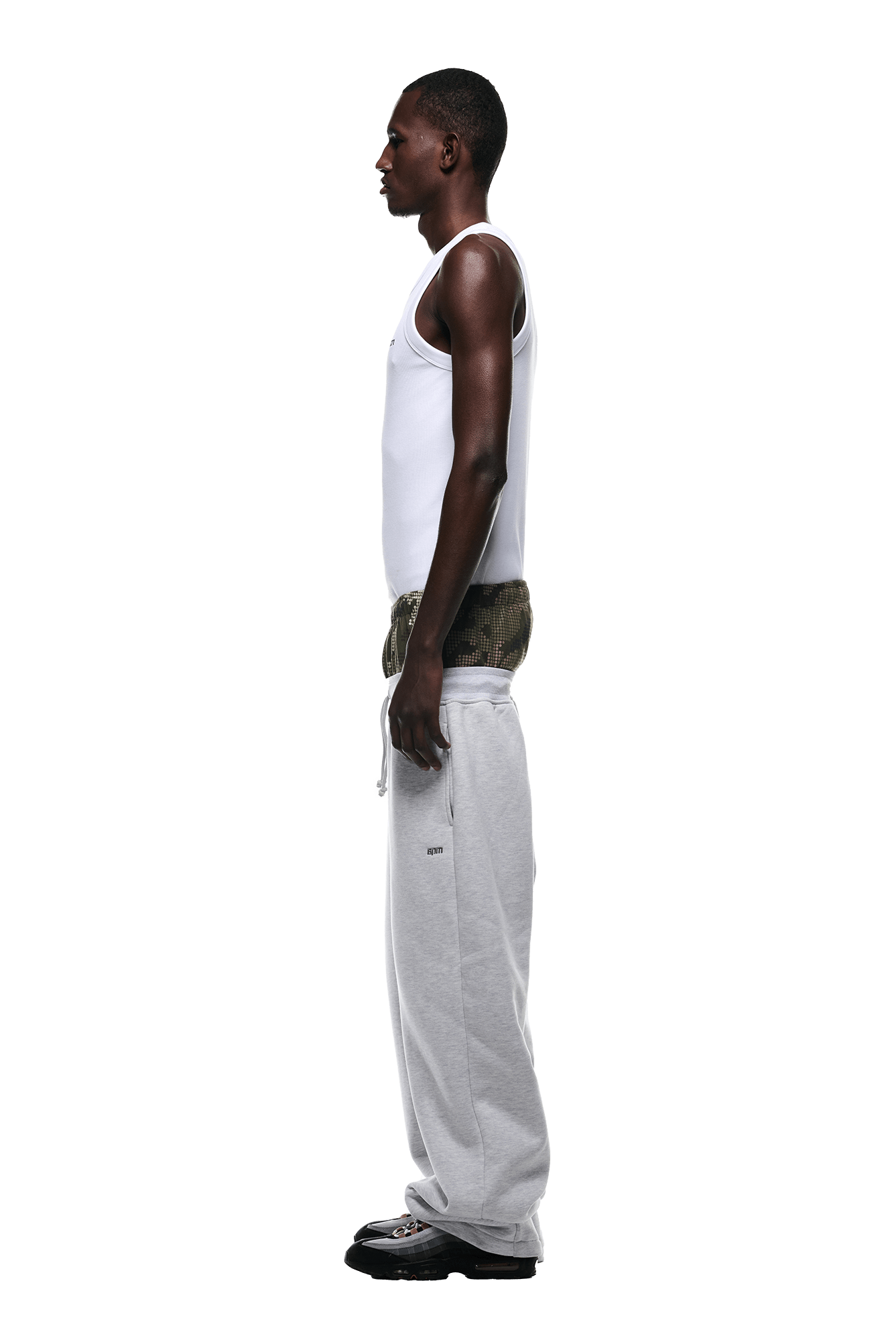 A man stands in profile against a plain background wearing 6PMs BOXERS OPEN LEG JOGGER GREY with a white tank top, camo boxers, and black shoes.
