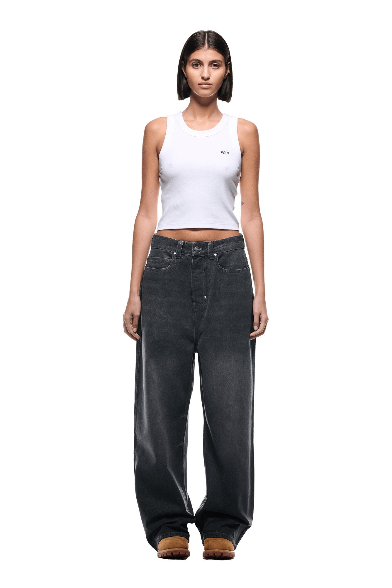 A woman stands facing forward against a plain white background, wearing a white cropped tank top, brown shoes, and 6PMs WAX COATED DENIM GREY jeans.
