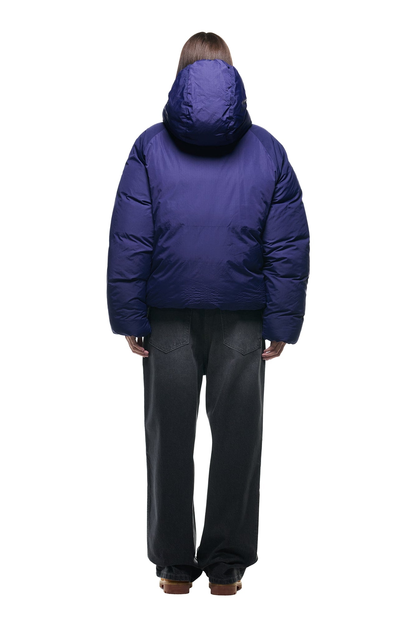 A person faces away, wearing the 6PM REVERSIBLE PUFFER JACKET BLUE with a hood and loose black jeans, set against a white background.