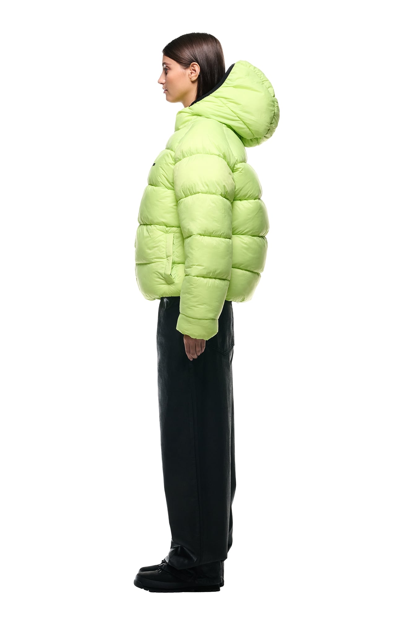 A woman stands in profile against a plain white background wearing the 6PM REVERSIBLE PUFFER JACKET BLACK, paired with black wide-leg pants and black shoes.