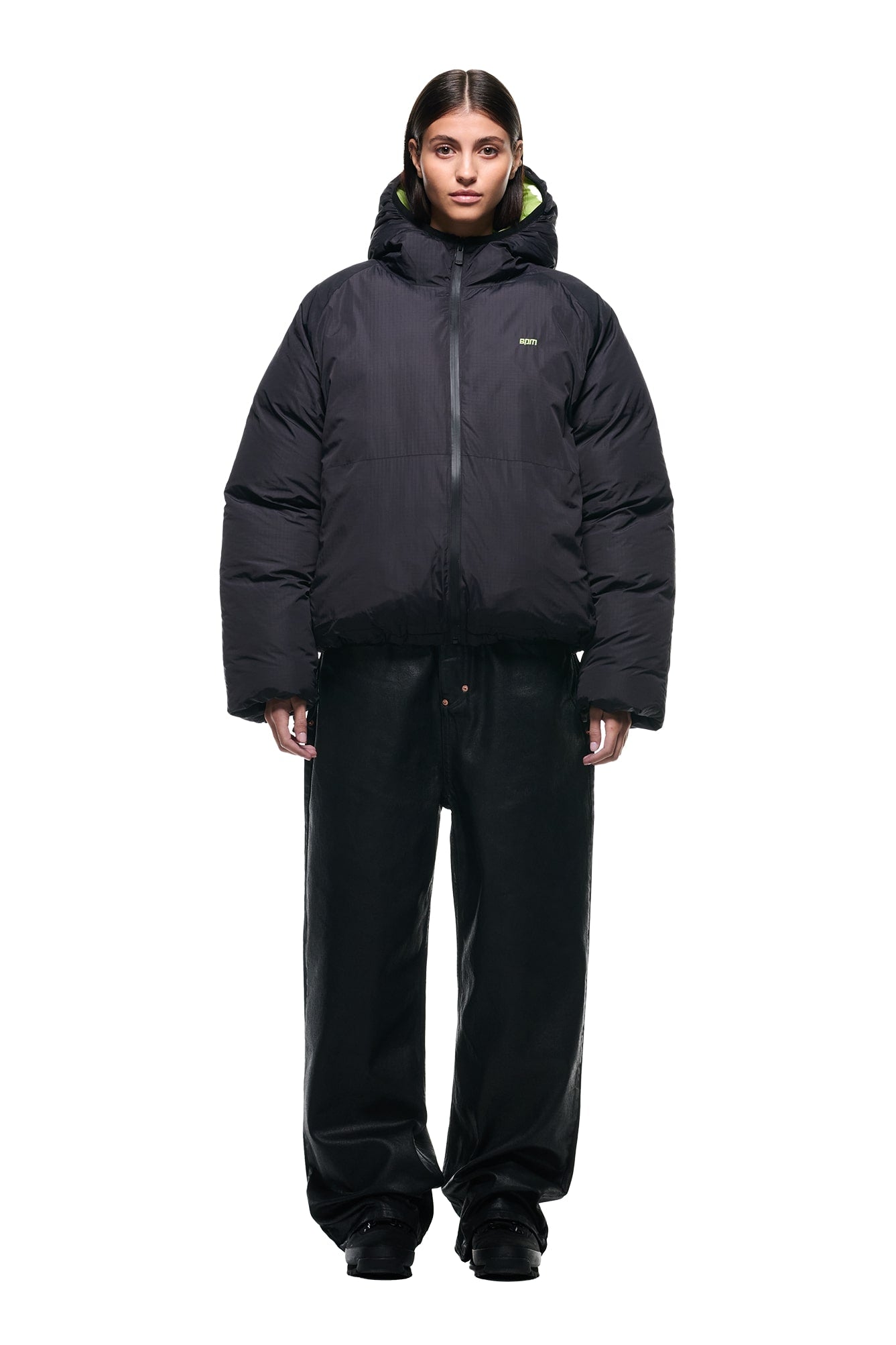 A person faces forward, wearing the 6PM REVERSIBLE PUFFER JACKET BLACK with a hood and loose black pants against a plain white background.