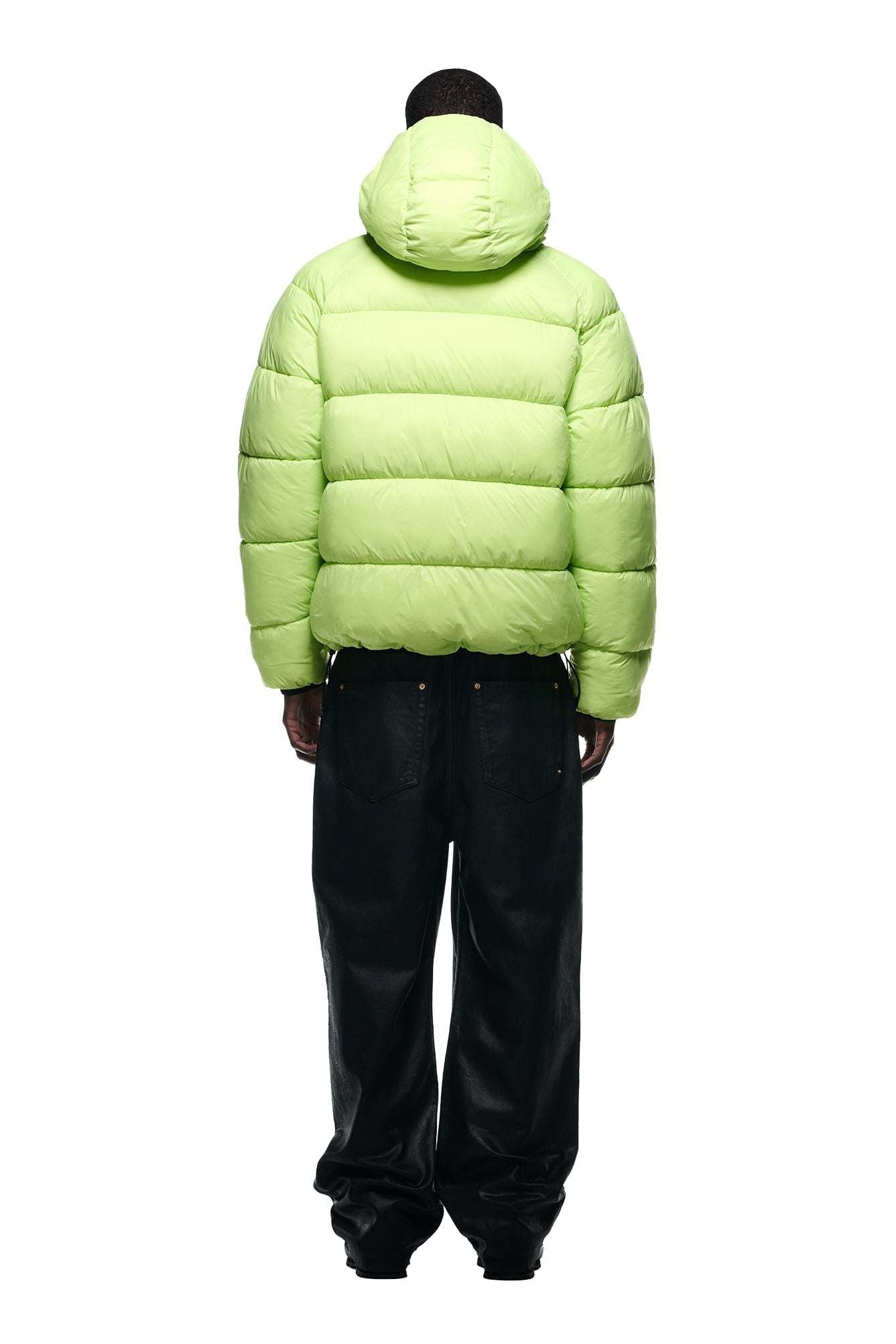 A person models the 6PM REVERSIBLE PUFFER JACKET BLACK with a hood and relaxed black pants, shown from the back against a white background.