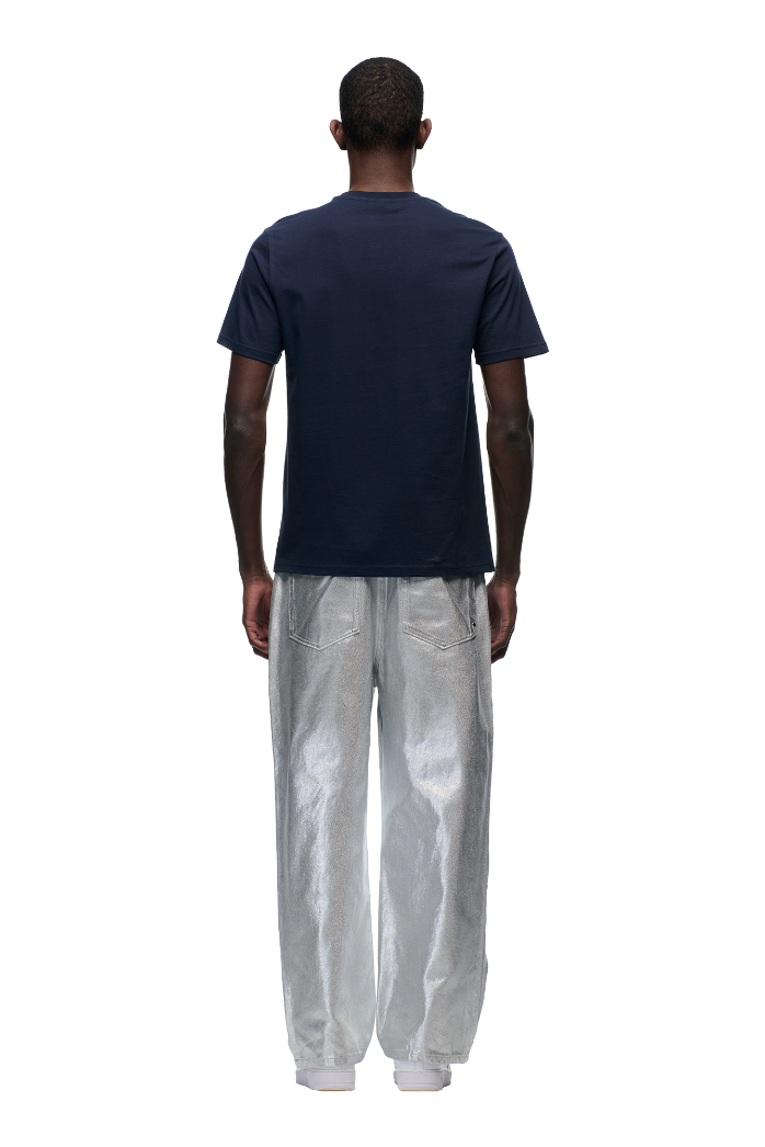 A person faces away from the camera, wearing the 6PM CLEAN EDGE WAVE T-SHIRT in MIDNIGHT BLUE with loose silver pants featuring back pockets, set against a plain white background.