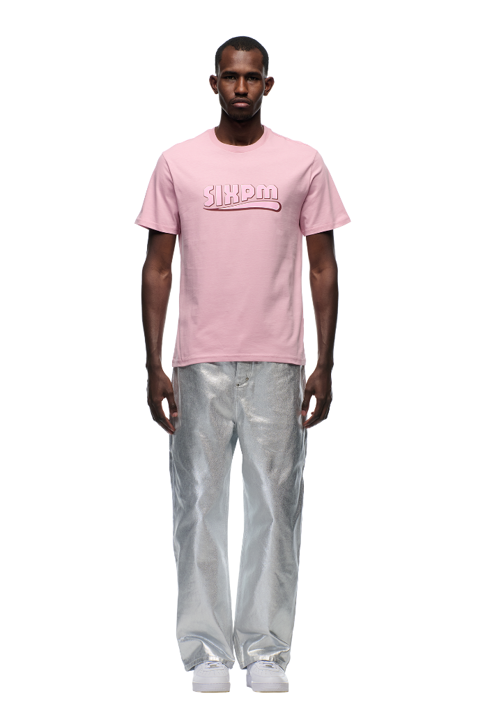 A man faces forward in a 6PM CLEAN EDGE WAVE T-SHIRT PINK with SHERM puff print, silver metallic pants, and white sneakers, set against a plain white background.