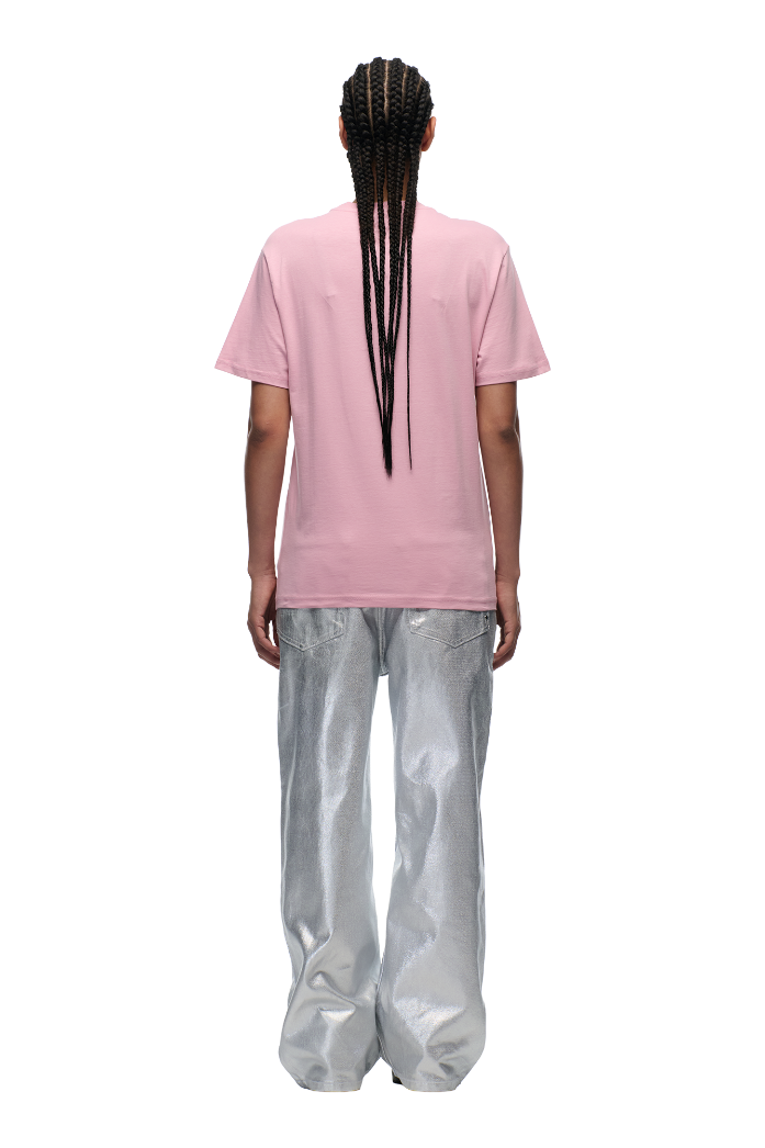 A person with long braids, seen from the back, wears the 6PM CLEAN EDGE WAVE T-SHIRT PINK paired with loose, shiny silver pants against a plain white background.