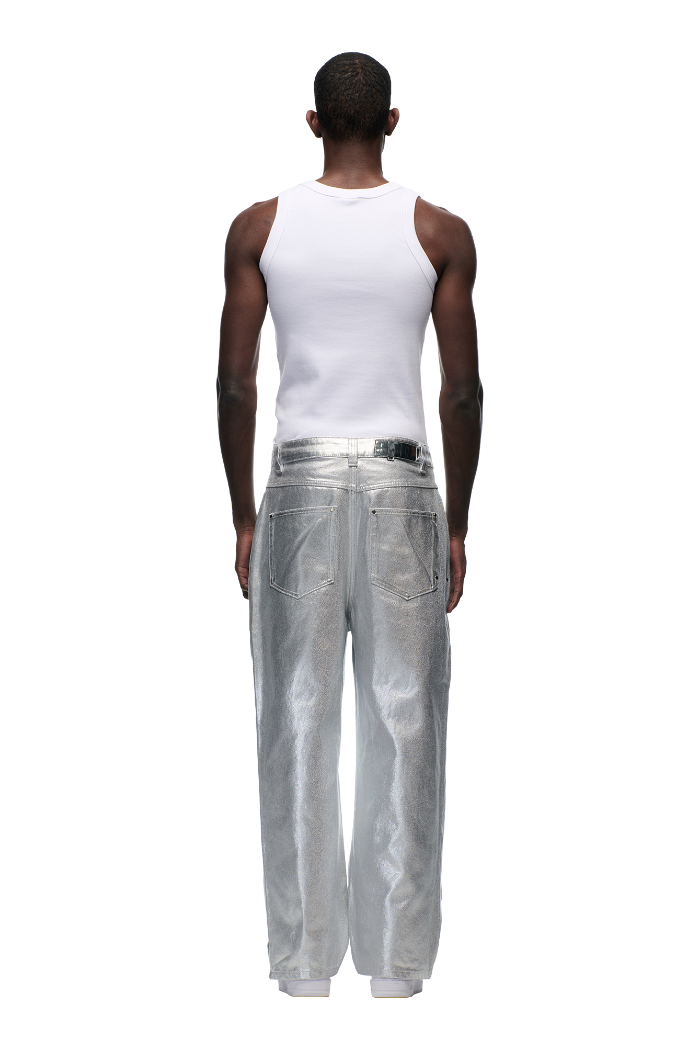 A person stands facing away, wearing a white sleeveless tank and 6PM's WAX COATED DENIM SILVER SURFER pants in shiny silver, set against a plain light gray background.
