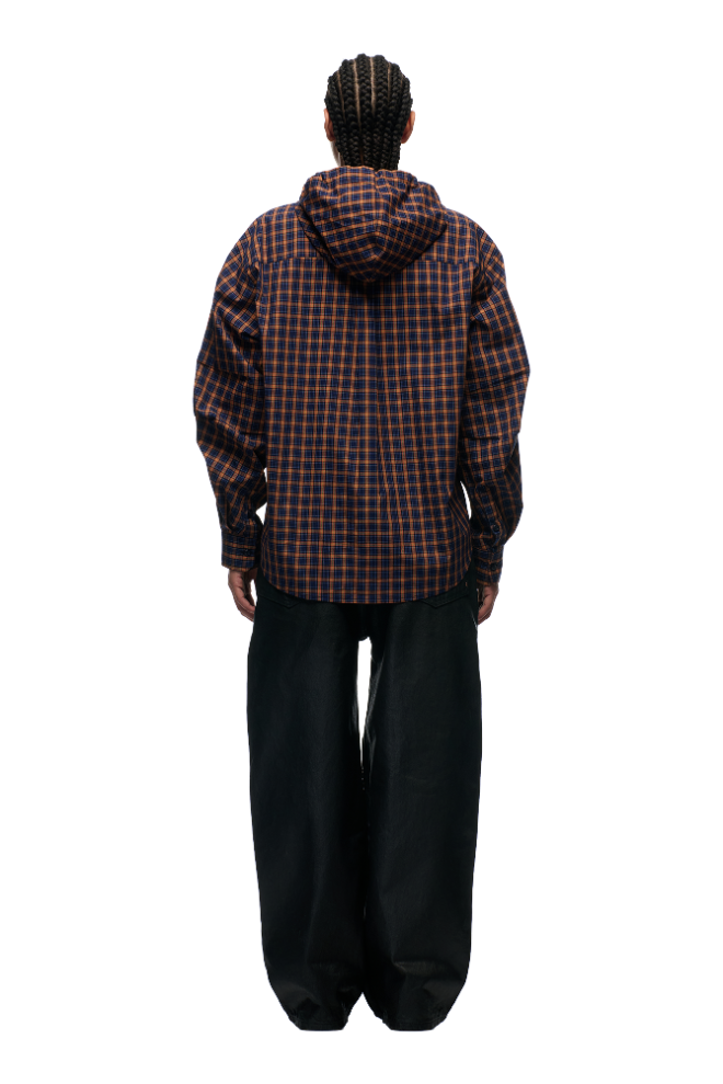 A person with braided hair faces away, wearing the 6PM HOODED DRESS SHIRT BLUE/ORANGE/BLACK and loose black pants against a plain light gray background.
