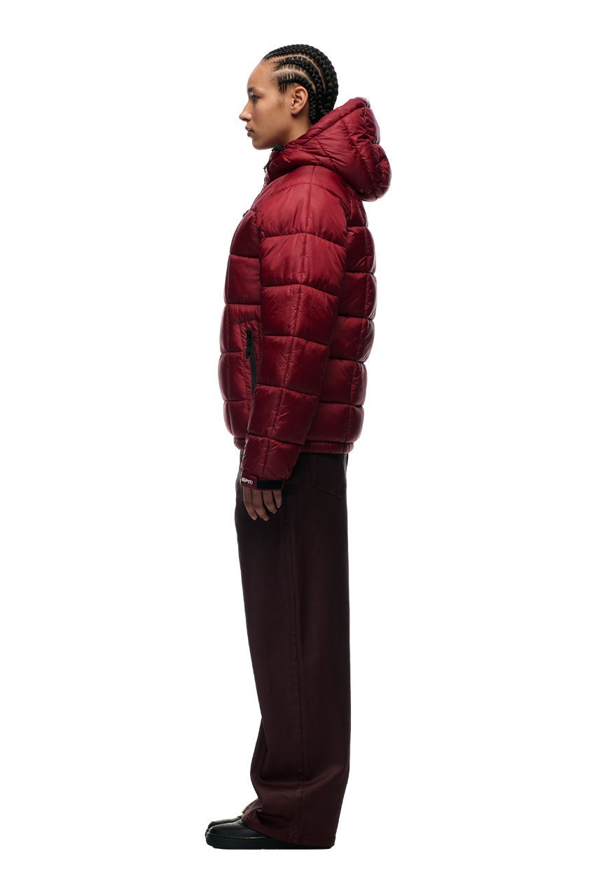 Person in profile against a white background wears the 6PM LIGHT PUFFER JACKET RECTANGLES WINE RED with adjustable hood, paired with loose dark pants and black shoes.