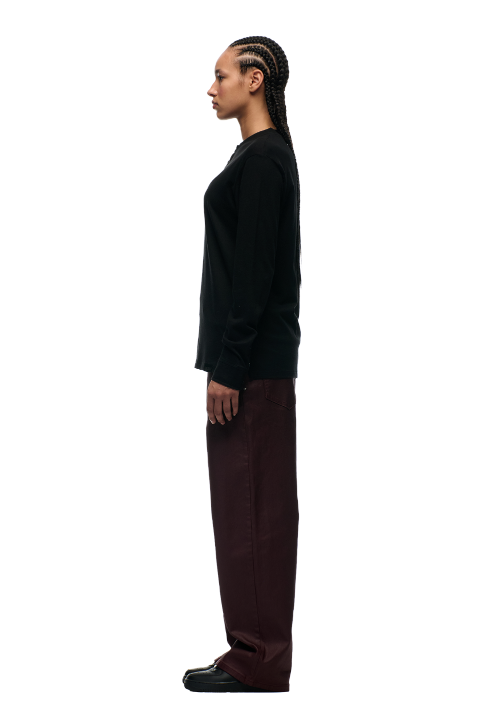 A person with long, braided hair stands in profile facing left, wearing the 6PM BUTTONED SLIM FIT LS BLACK shirt, paired with loose maroon pants and black shoes, set against a plain white background.