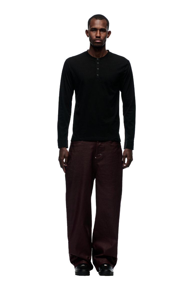 A man faces forward wearing the 6PM BUTTONED SLIM FIT LS BLACK shirt, styled with loose dark brown pants and black shoes, set against a plain light gray background.