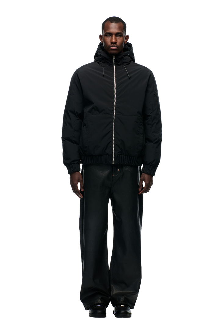 A man faces forward against a light gray background, wearing the 6PM EMBOSSED JACKET BLACK with detachable balaclava, wide-leg black pants, and black shoes.