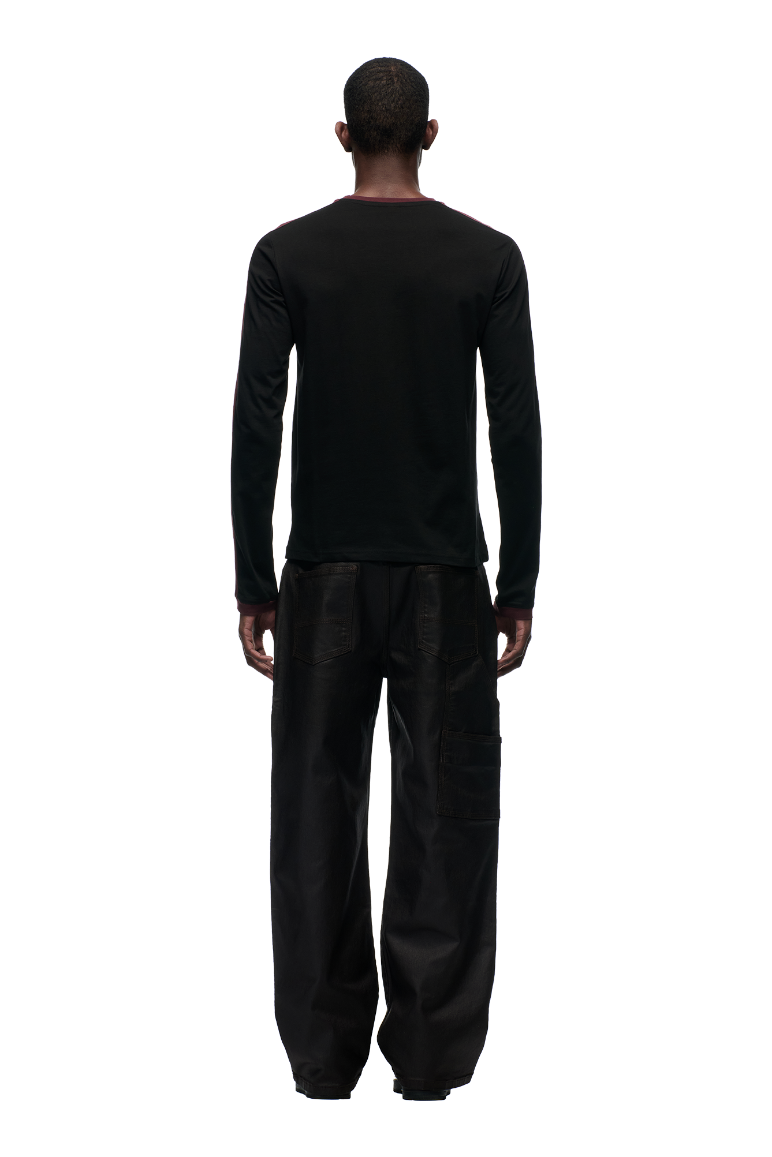 A person with short hair faces away from the camera, wearing the 6PM GRAFFITI RINGER LS BLACK top and loose black cargo pants against a plain light gray background.