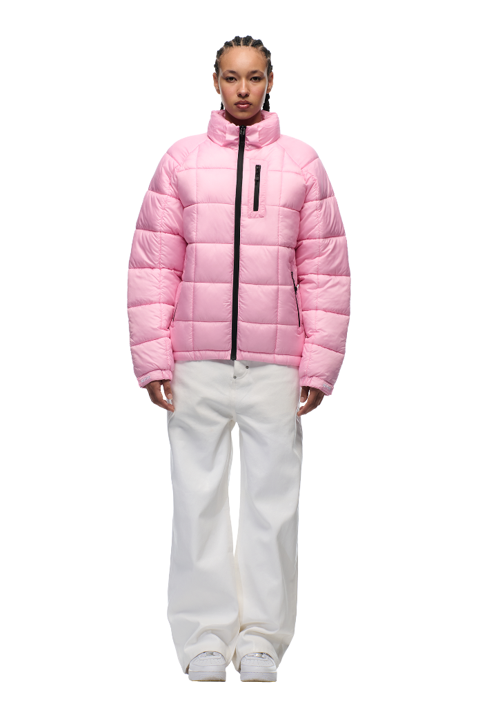 A person wears the 6PM LIGHT PUFFER JACKET RECTANGLES PINK, featuring an adjustable hood and zippered chest pocket, styled with loose white pants and white sneakers, standing against a plain white background.
