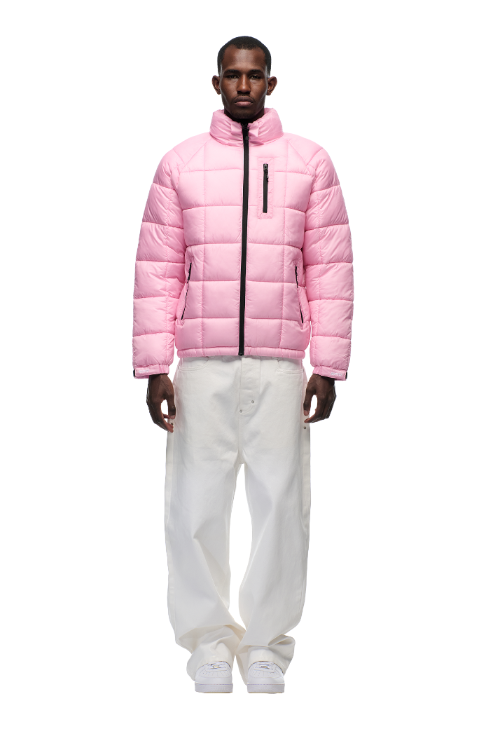 A man faces forward in a 6PM LIGHT PUFFER JACKET RECTANGLES PINK with a high collar and black zipper, paired with loose white pants and white sneakers, all set against a plain white background.