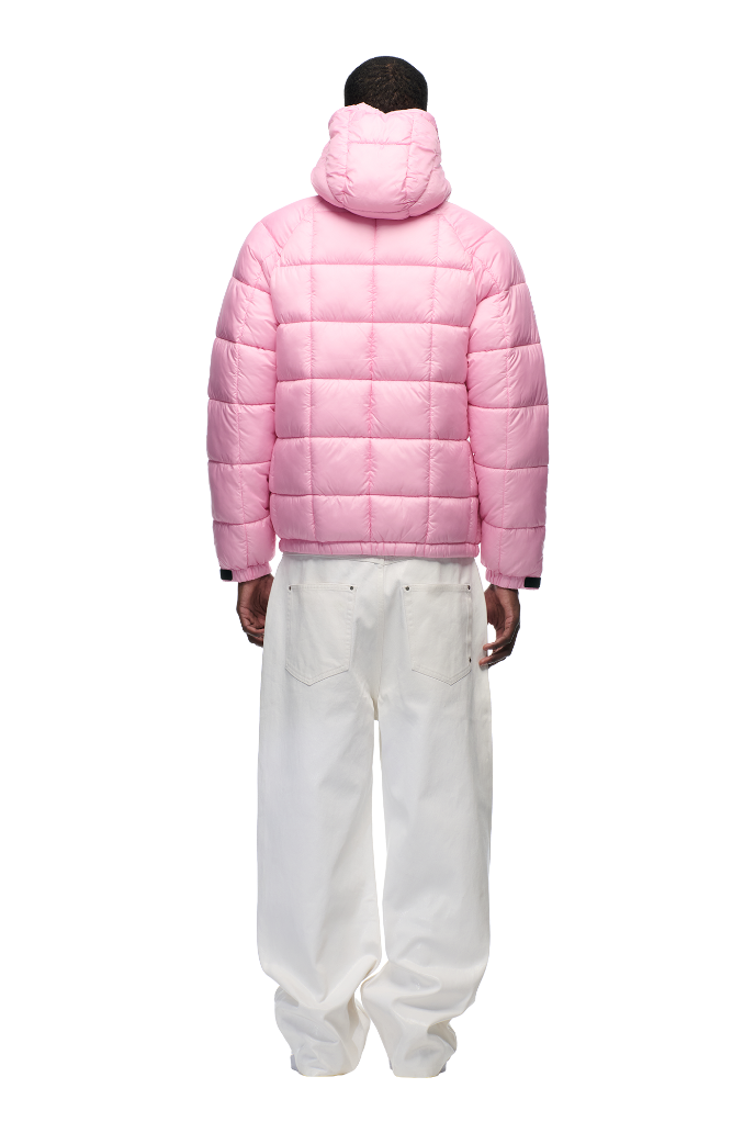 A person faces away, wearing the 6PM LIGHT PUFFER JACKET RECTANGLES PINK with an adjustable hood, paired with loose white pants against a plain white background.