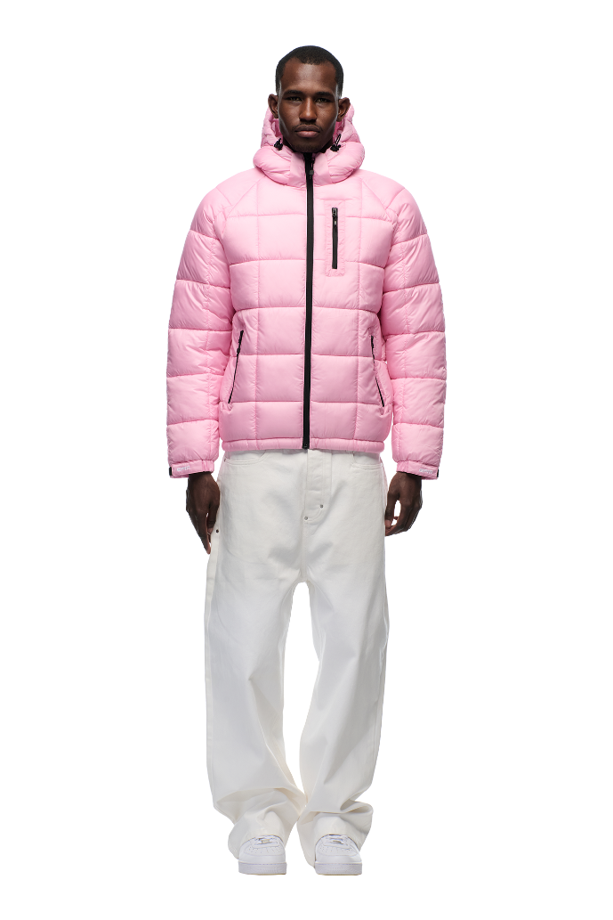 A man faces forward wearing the 6PM LIGHT PUFFER JACKET RECTANGLES PINK with an adjustable hood and black zippers, paired with baggy white pants and white sneakers, set against a plain white background.